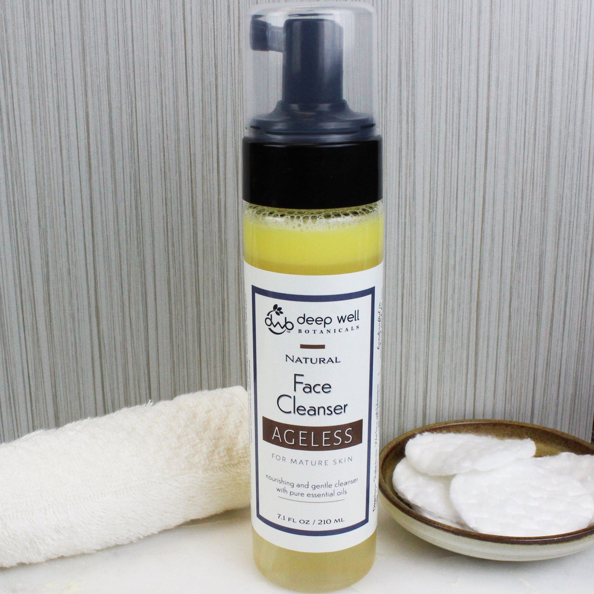 Face cleanser bottle with yellow liquid, black pump, and Deep Well Botanicals label next to a white washcloth