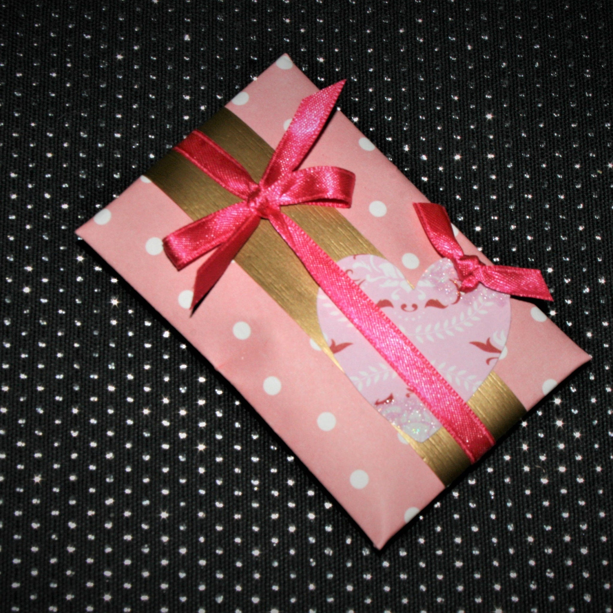 Gift box with pink polka dot paper, gold ribbon, and red bow on black background