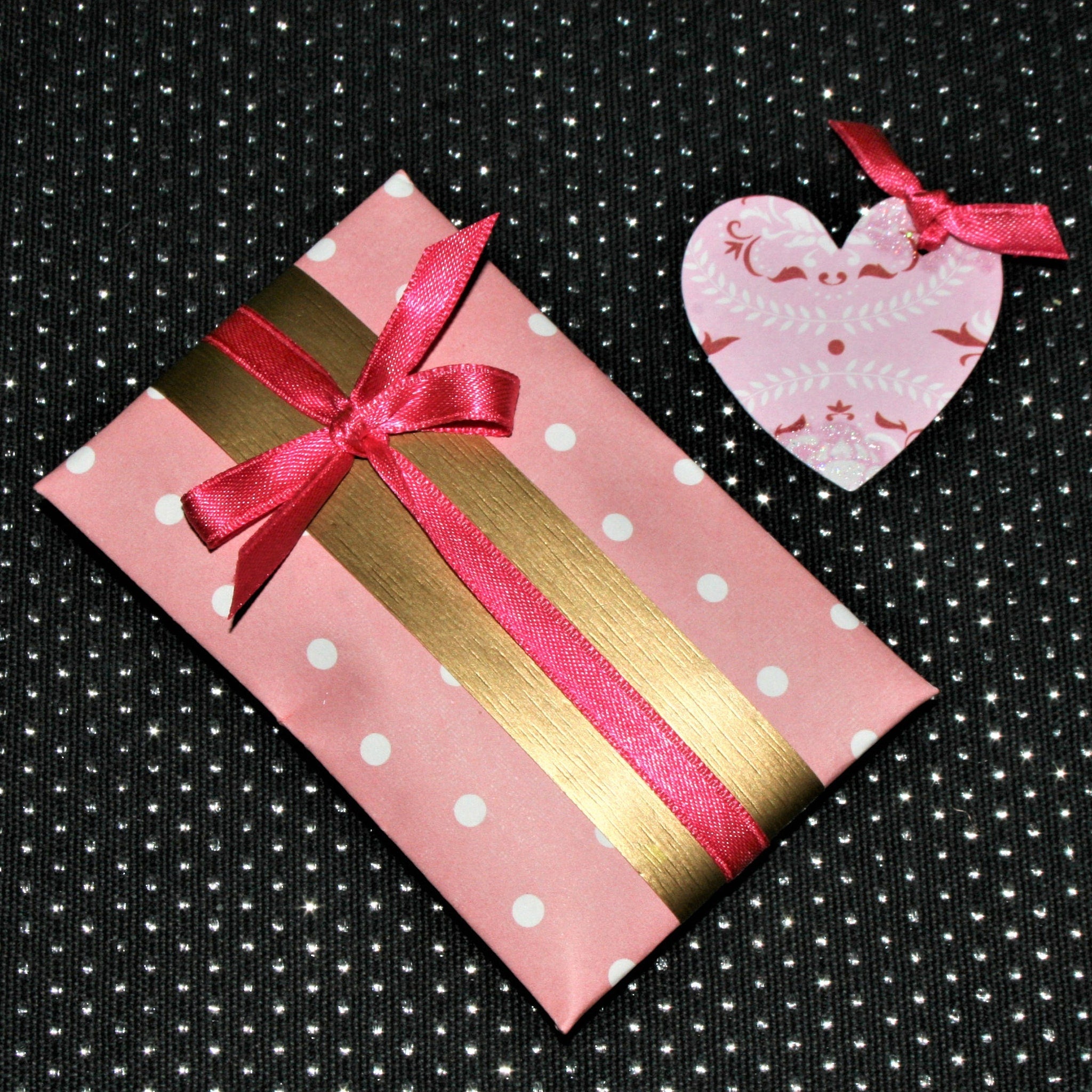 Pink polka dot gift box with gold ribbon and pink bow on black background