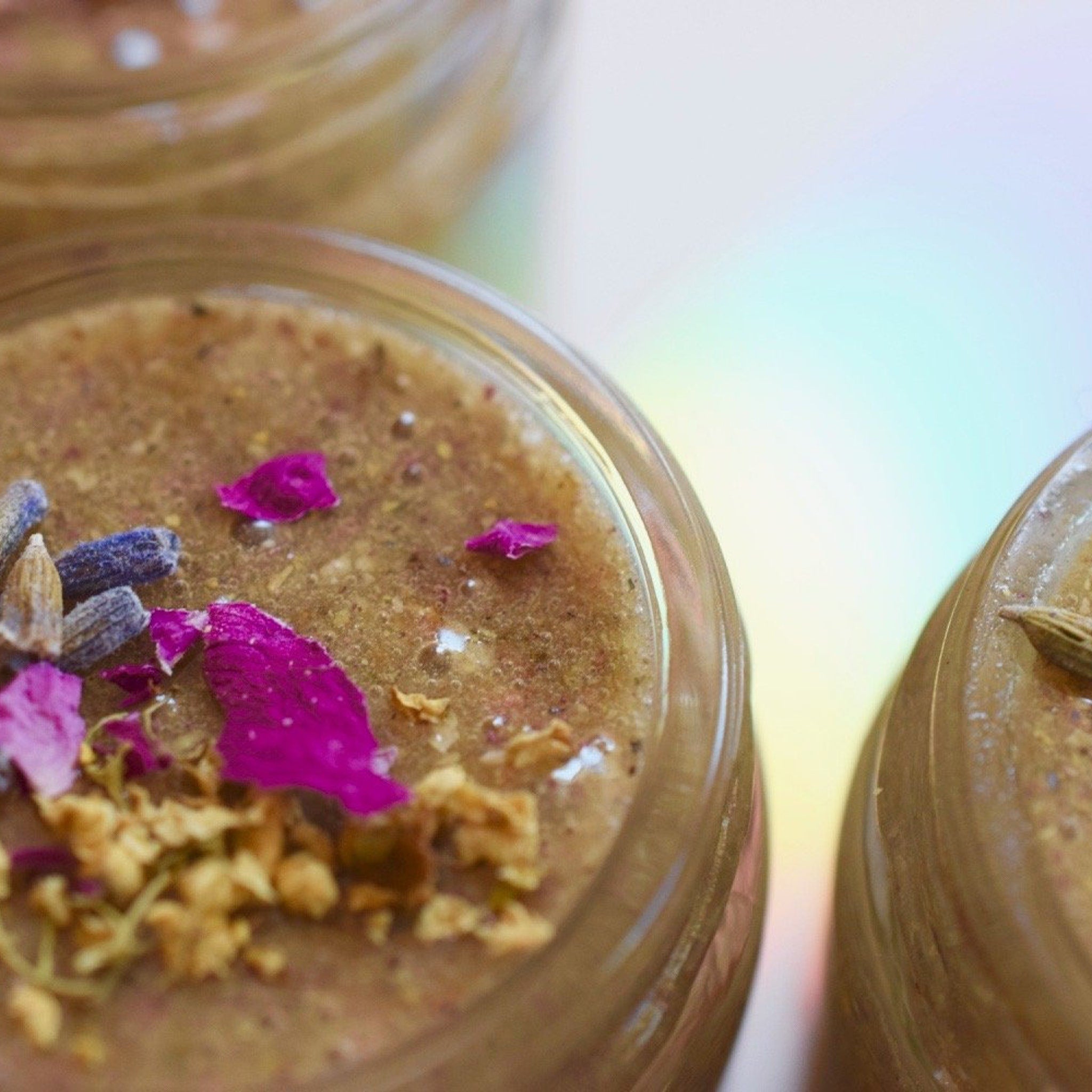 Body scrub with brown granules, pink petals, and glass jar details