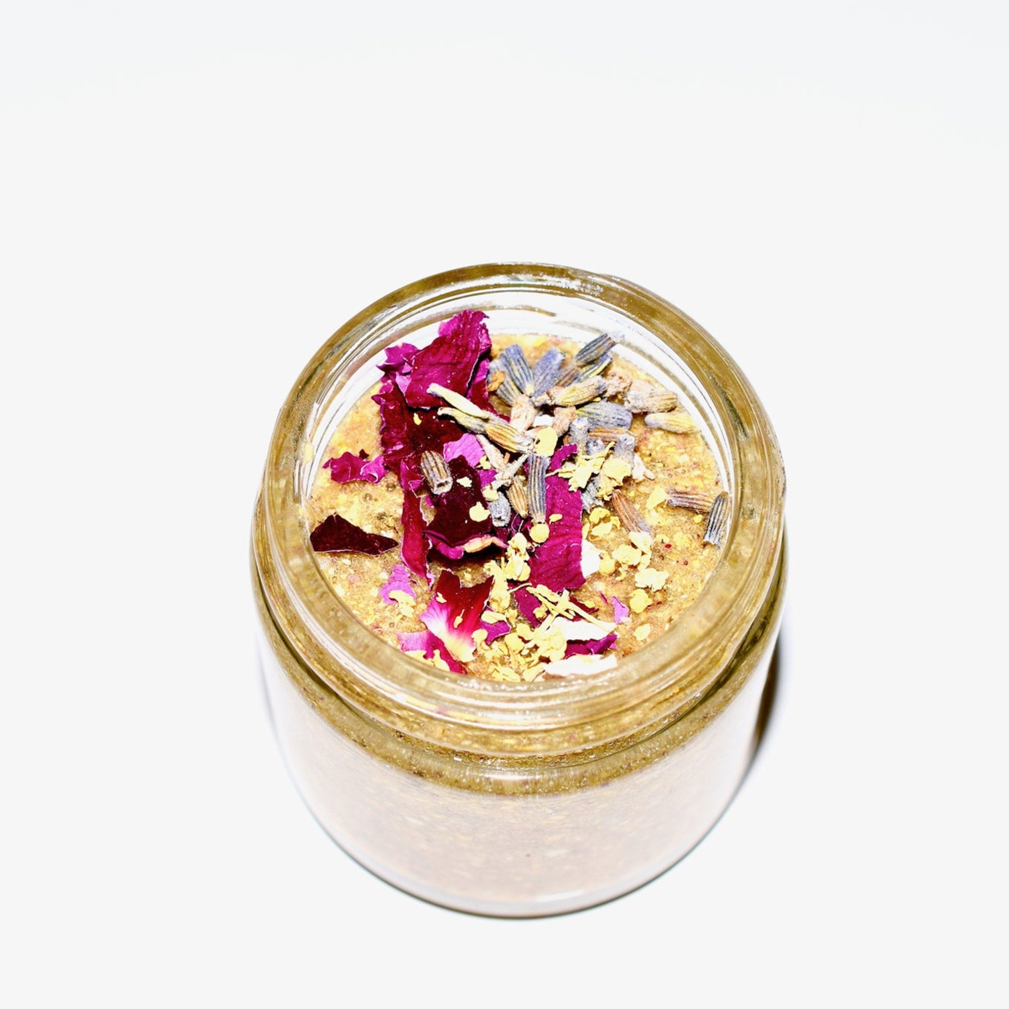 Jar of golden scrub with pink petals and purple lavender buds, clear glass container