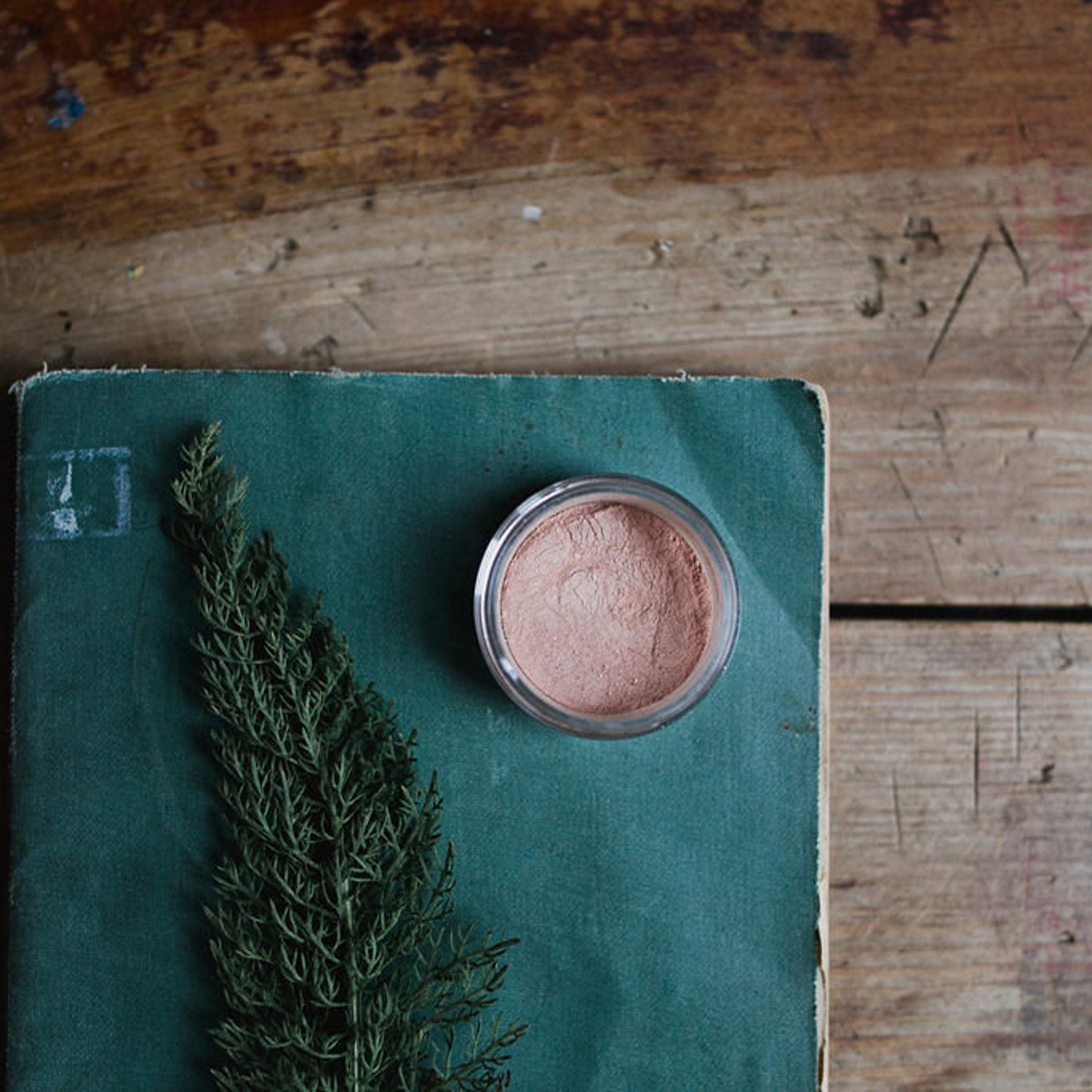Side view of loose mineral eye shadow powder in glass jar with metallic lid, showcasing texture and vegan label details