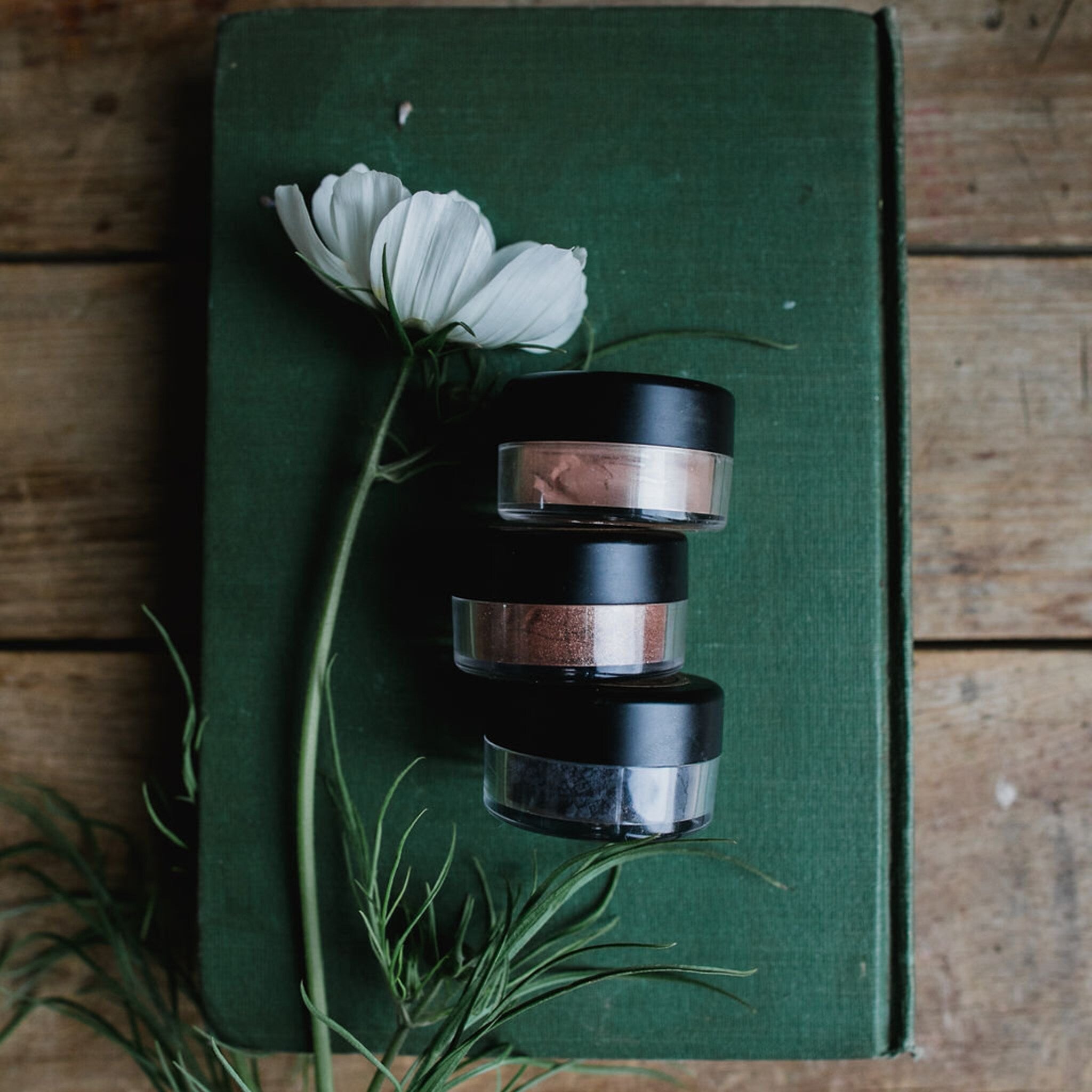 Stacked jars of Planet Wise vegan mineral eye shadows in assorted earthy tones with gold lids