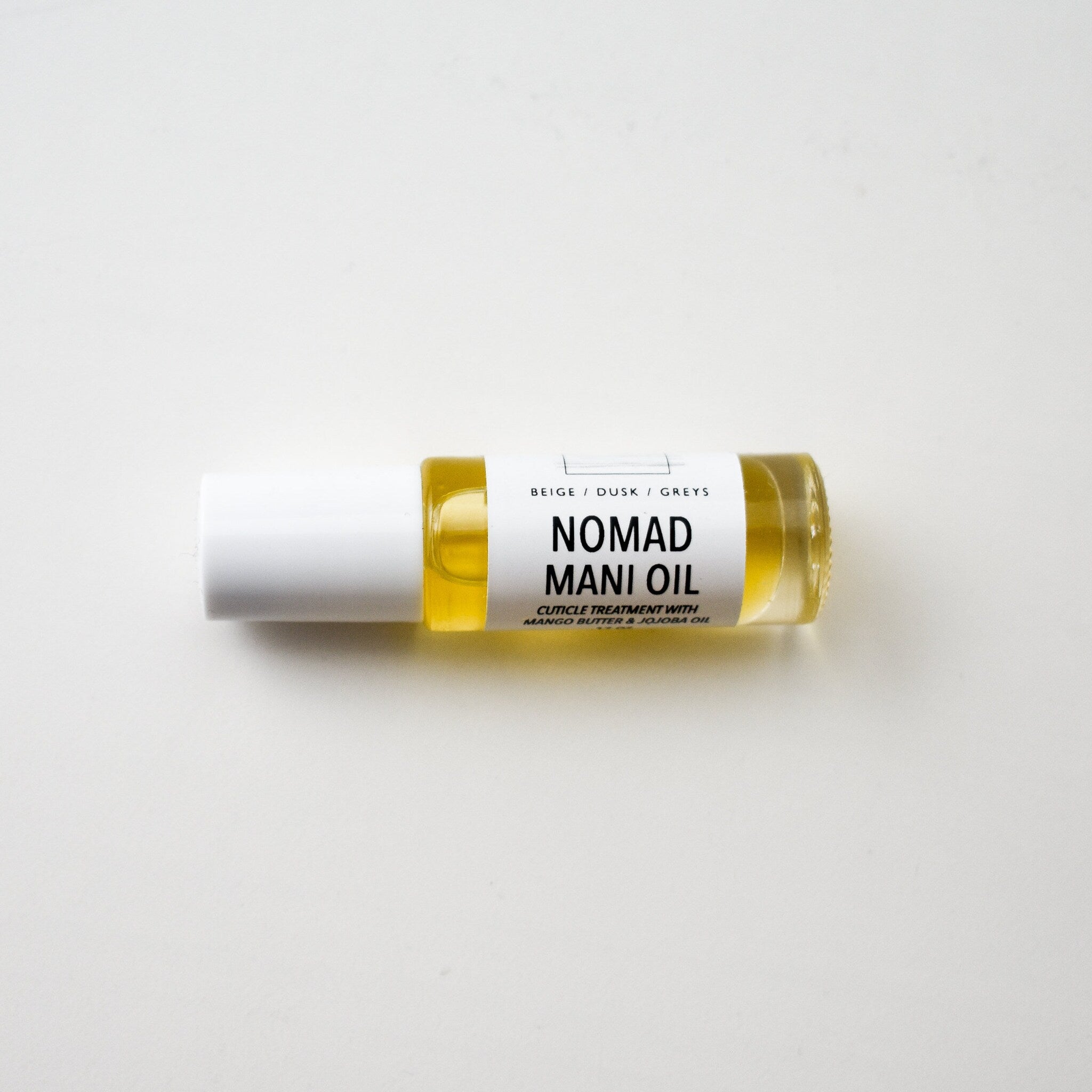 Mani oil bottle with white cap, clear glass, and Nomad label on white background