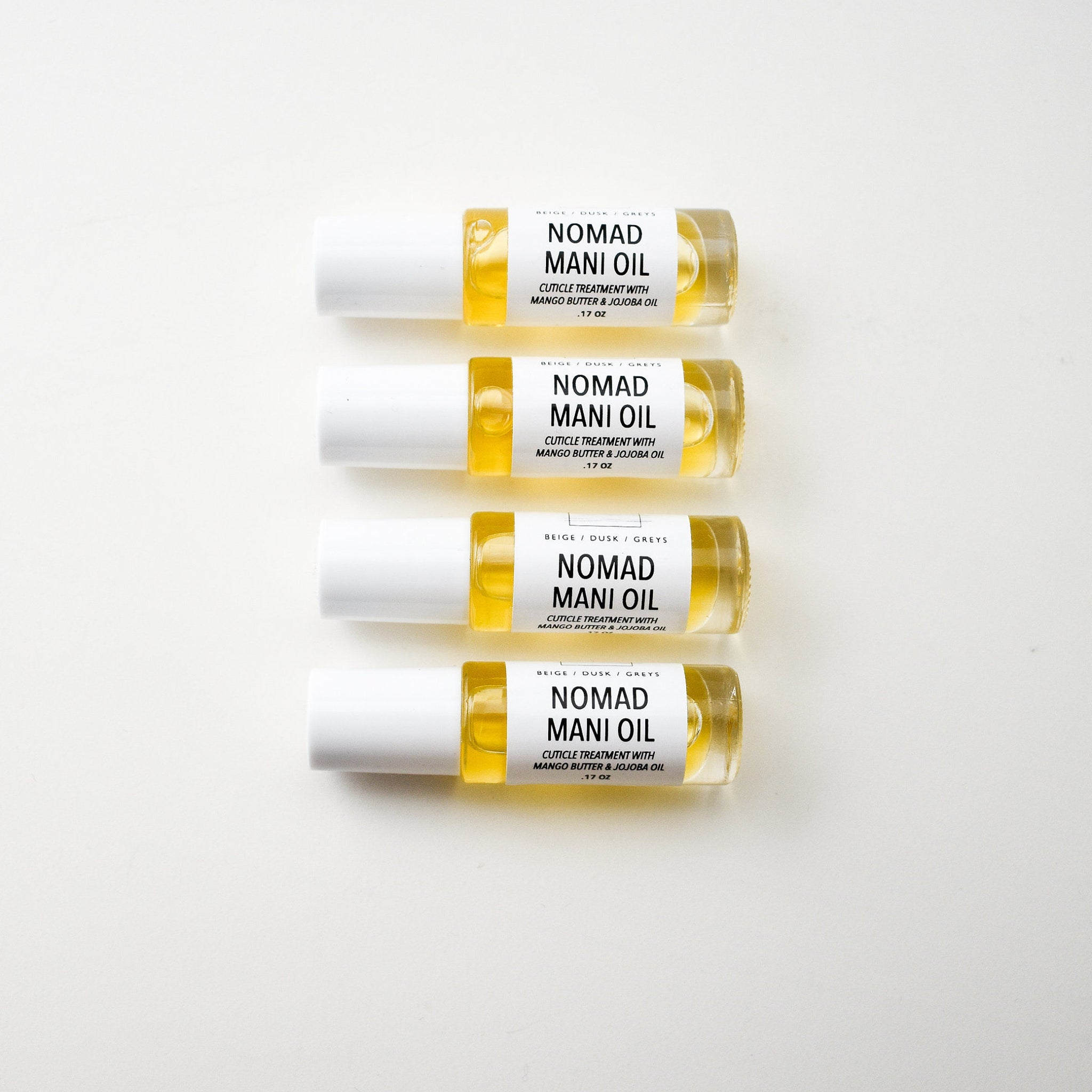 Cuticle oil bottles with clear glass, yellow liquid, and white cap, Nomad Mani Oil brand