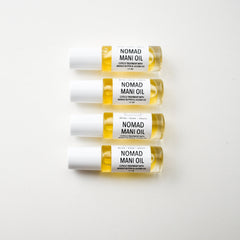 Cuticle oil bottles with clear glass, yellow liquid, and white cap, Nomad Mani Oil brand