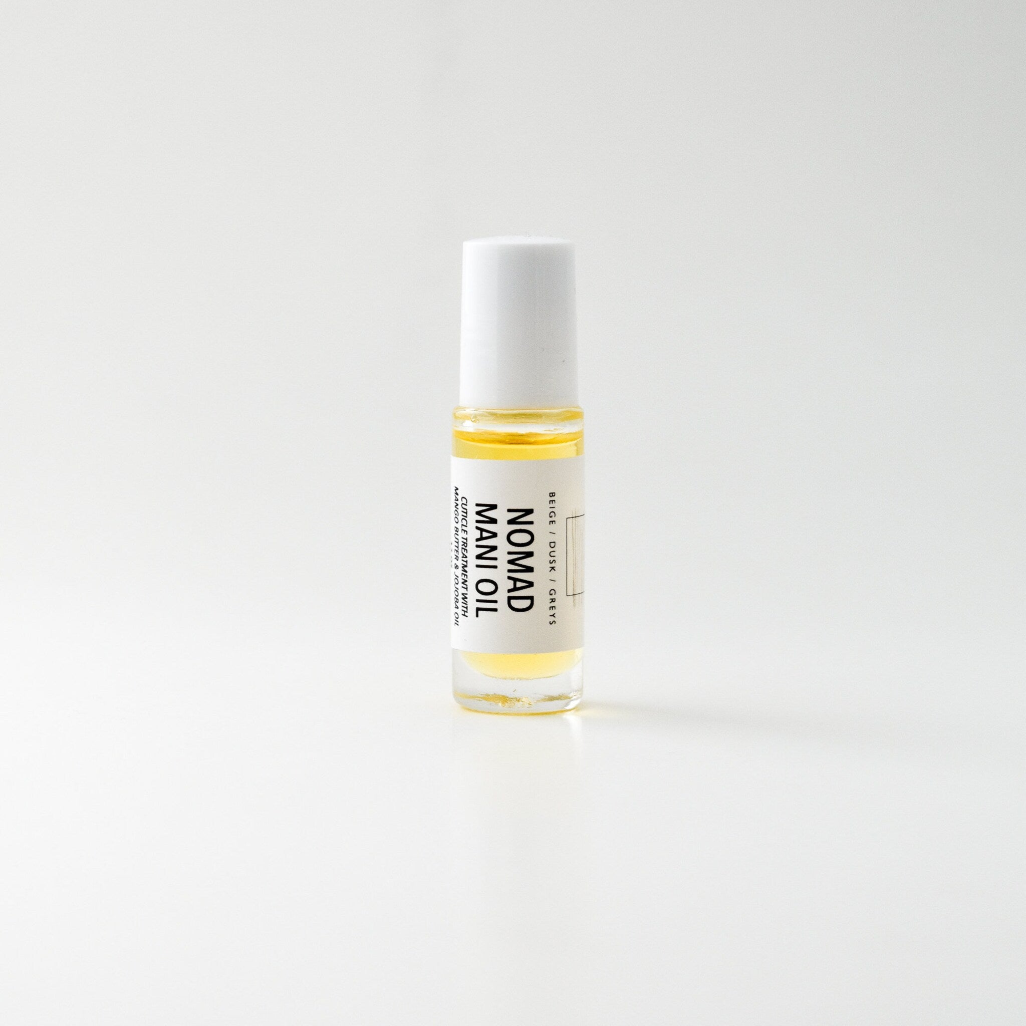 Mani oil bottle with white cap, clear glass, and yellow liquid, Nomad brand visible