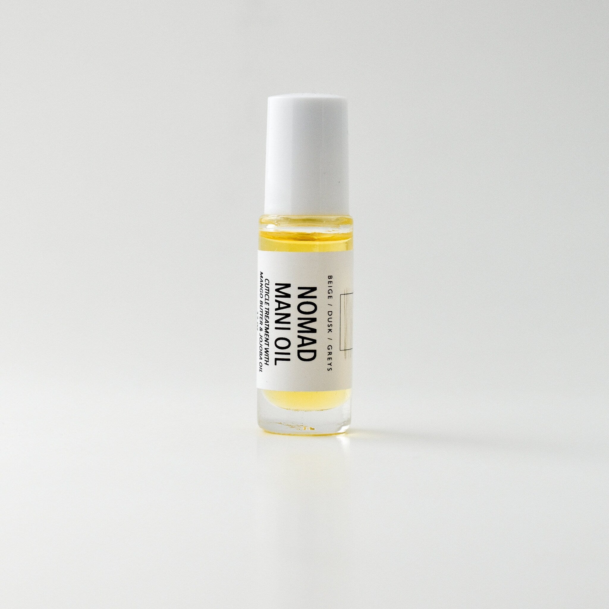 Mani oil bottle with white cap, clear glass, and yellow liquid, Nomad brand visible