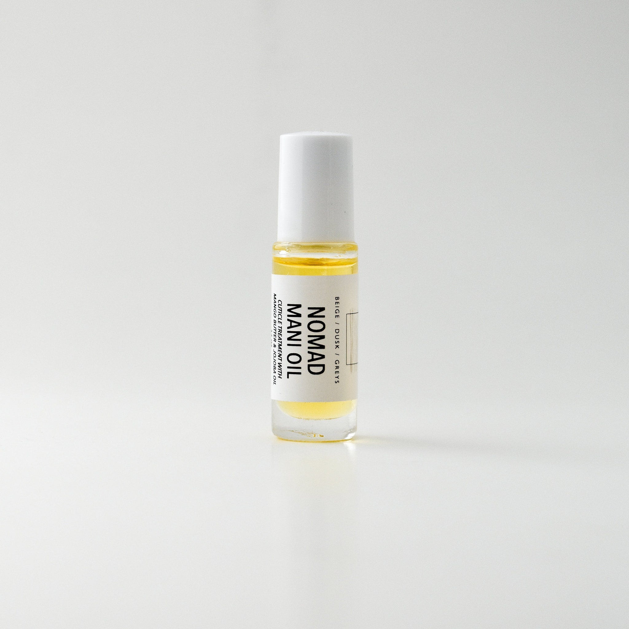 Mani oil bottle with white cap, clear glass, and yellow liquid, Nomad brand visible