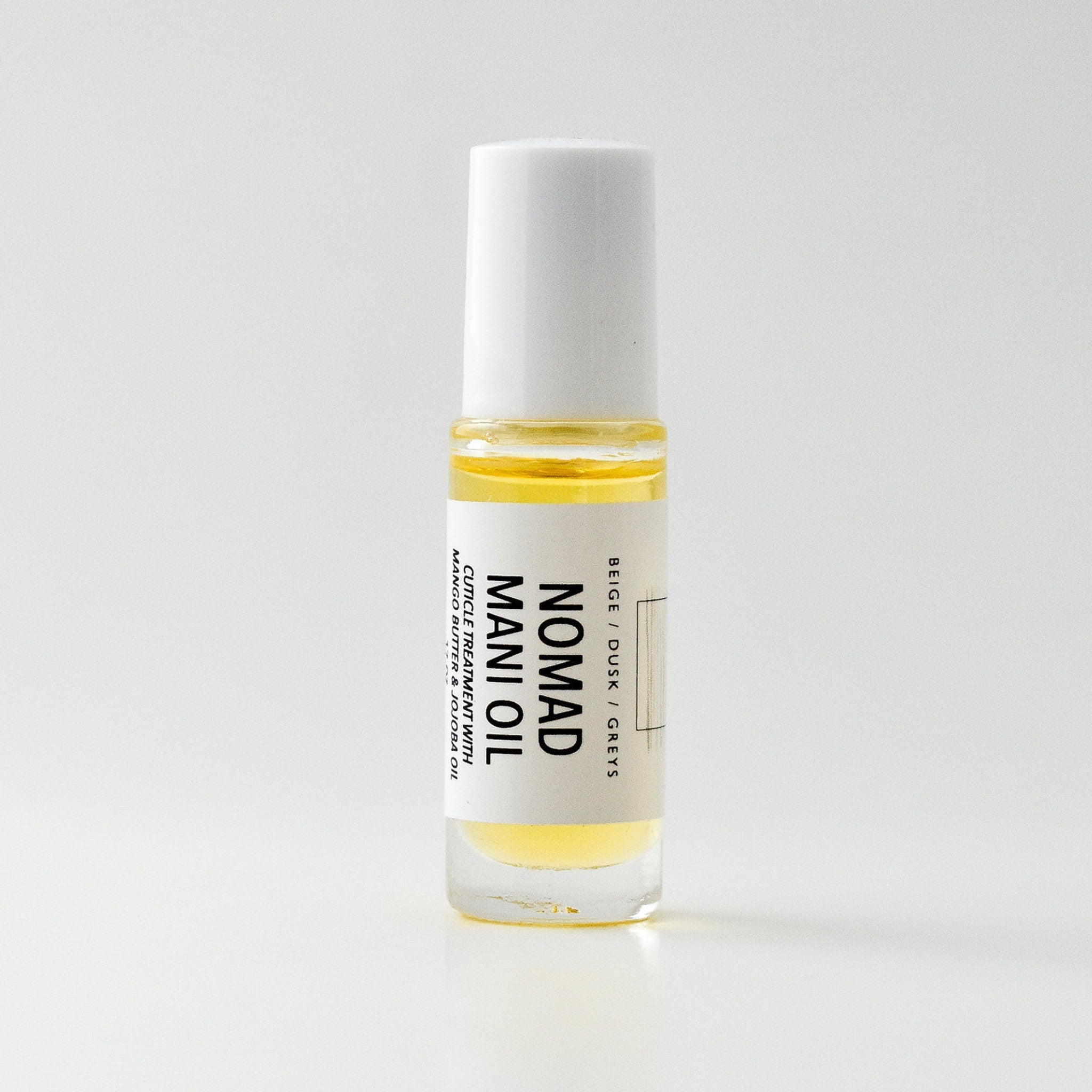 Mani oil bottle with white cap, clear glass, and yellow liquid, Nomad brand visible