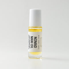 Mani oil bottle with white cap, clear glass, and yellow liquid, Nomad brand visible