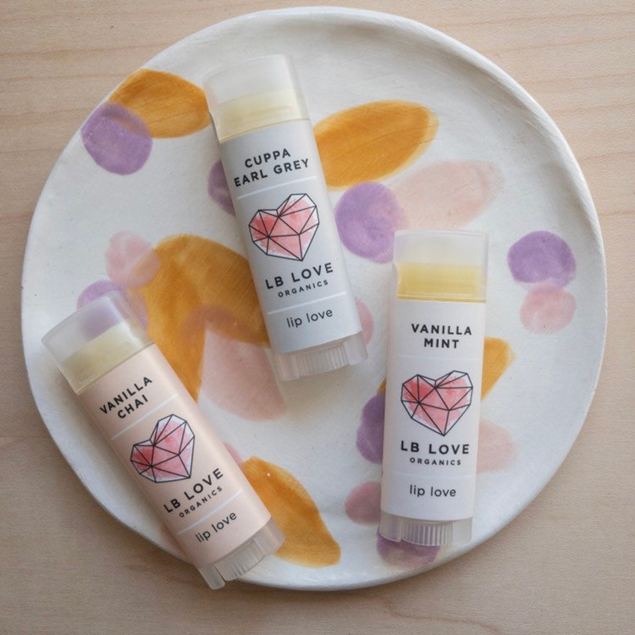 Lip balm tubes with white, pink, and gray labels, LB Love brand, on a painted plate