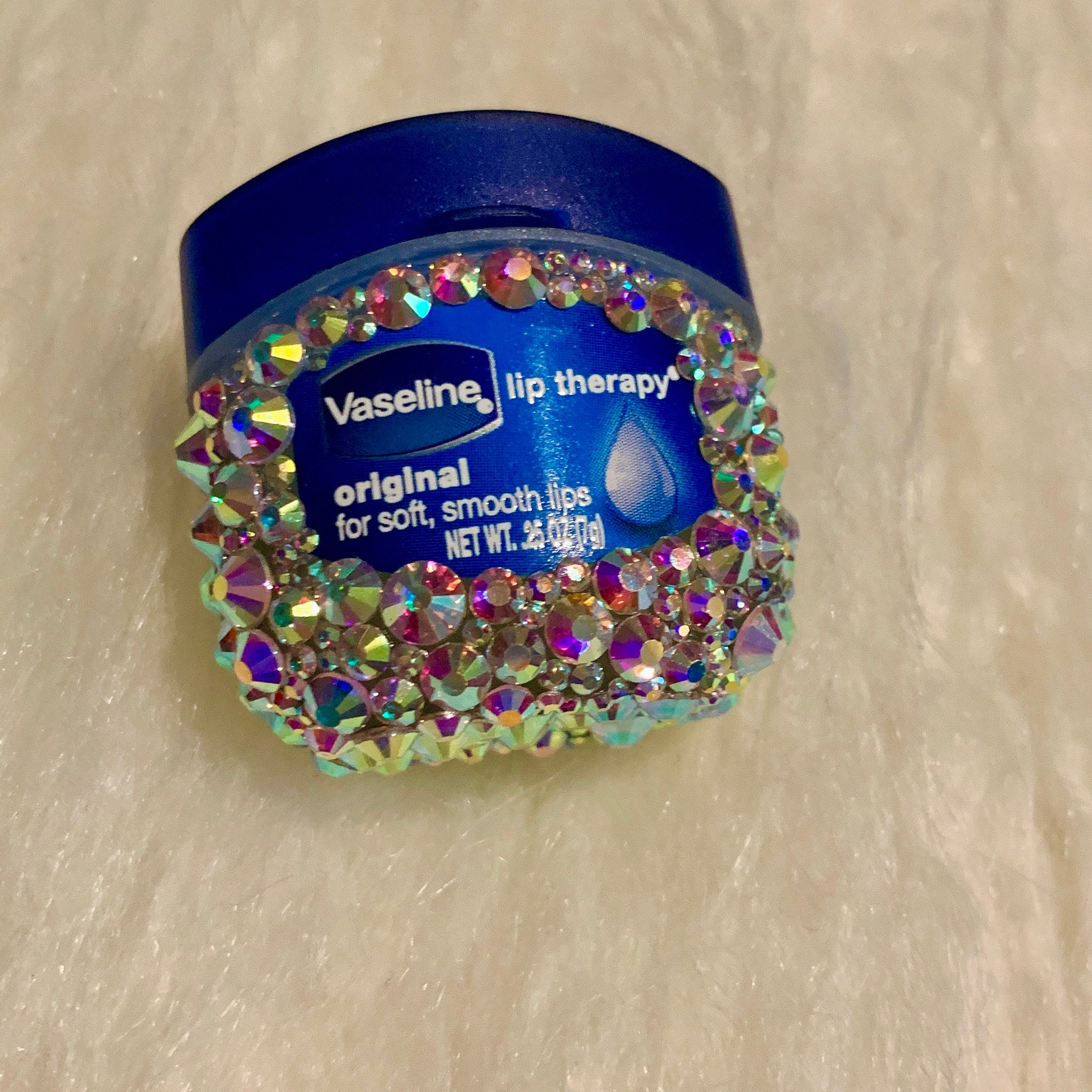 Lip therapy jar with blue lid, iridescent gems, and Vaseline label on white fabric