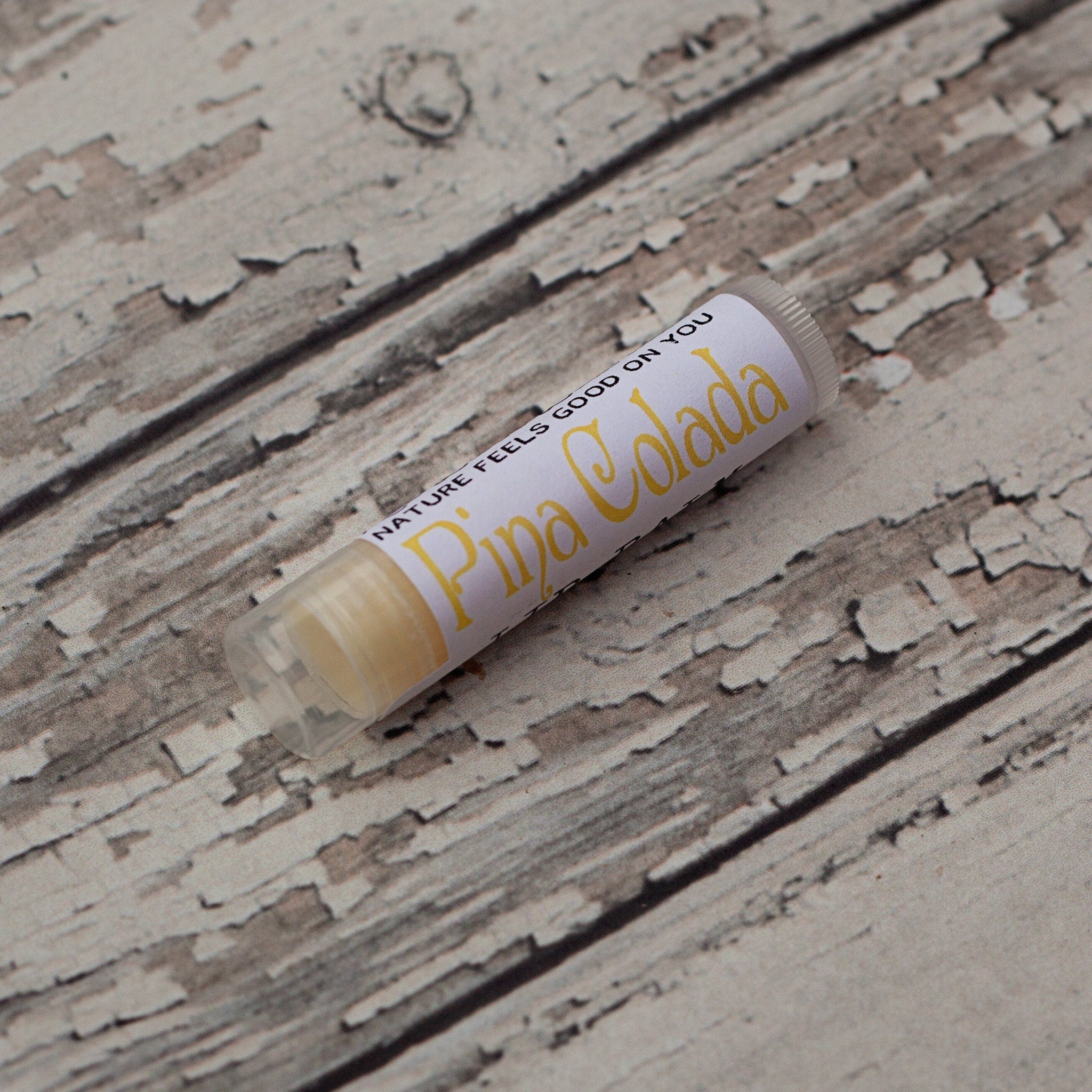 Lip balm tube with yellow text on white label, clear plastic tube, on wood background