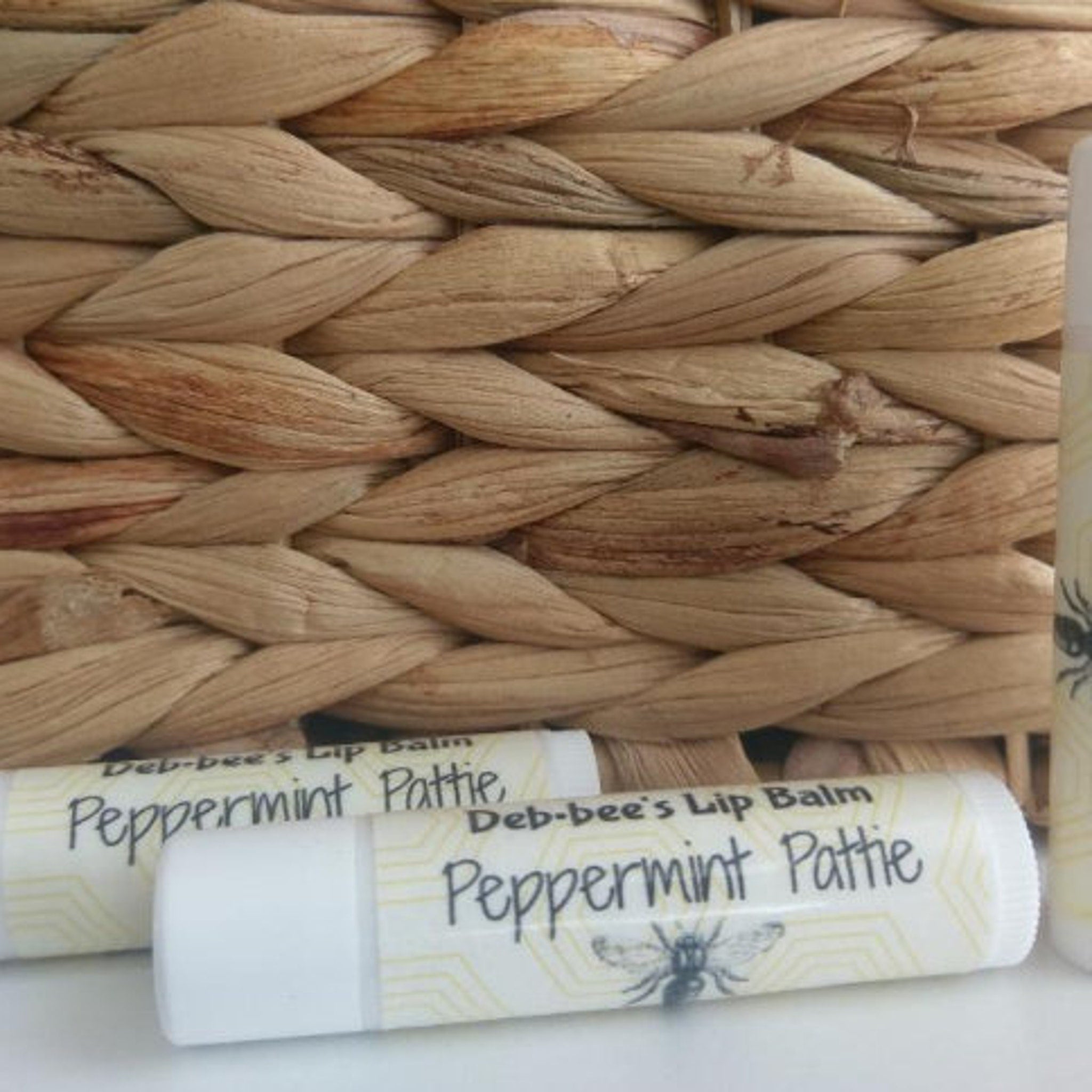 Lip balm tubes, white with yellow pattern, Deb*bee's Peppermint Pattie text, near woven basket