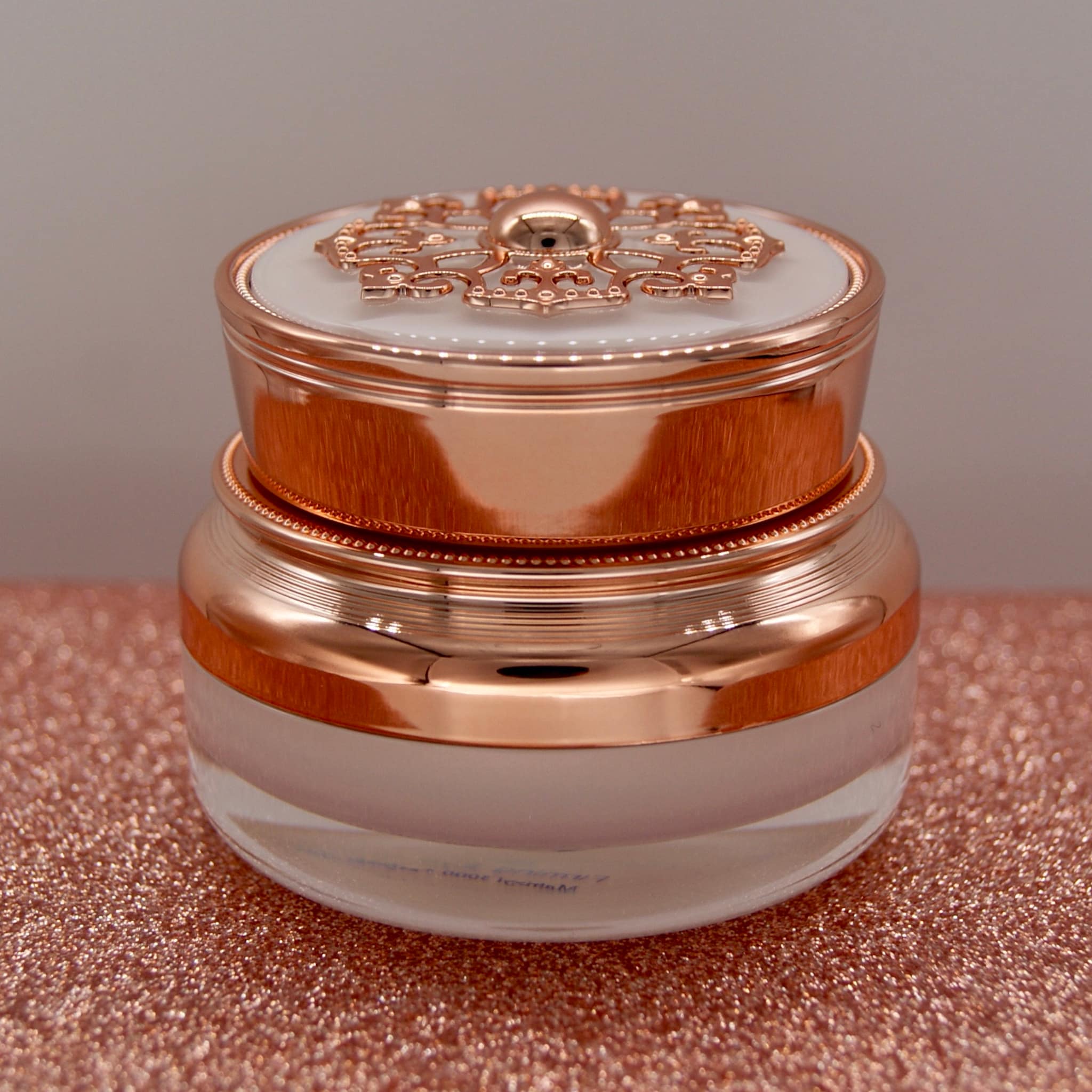 Cosmetic jar with rose gold metallic finish, ornate lid, and clear glass base