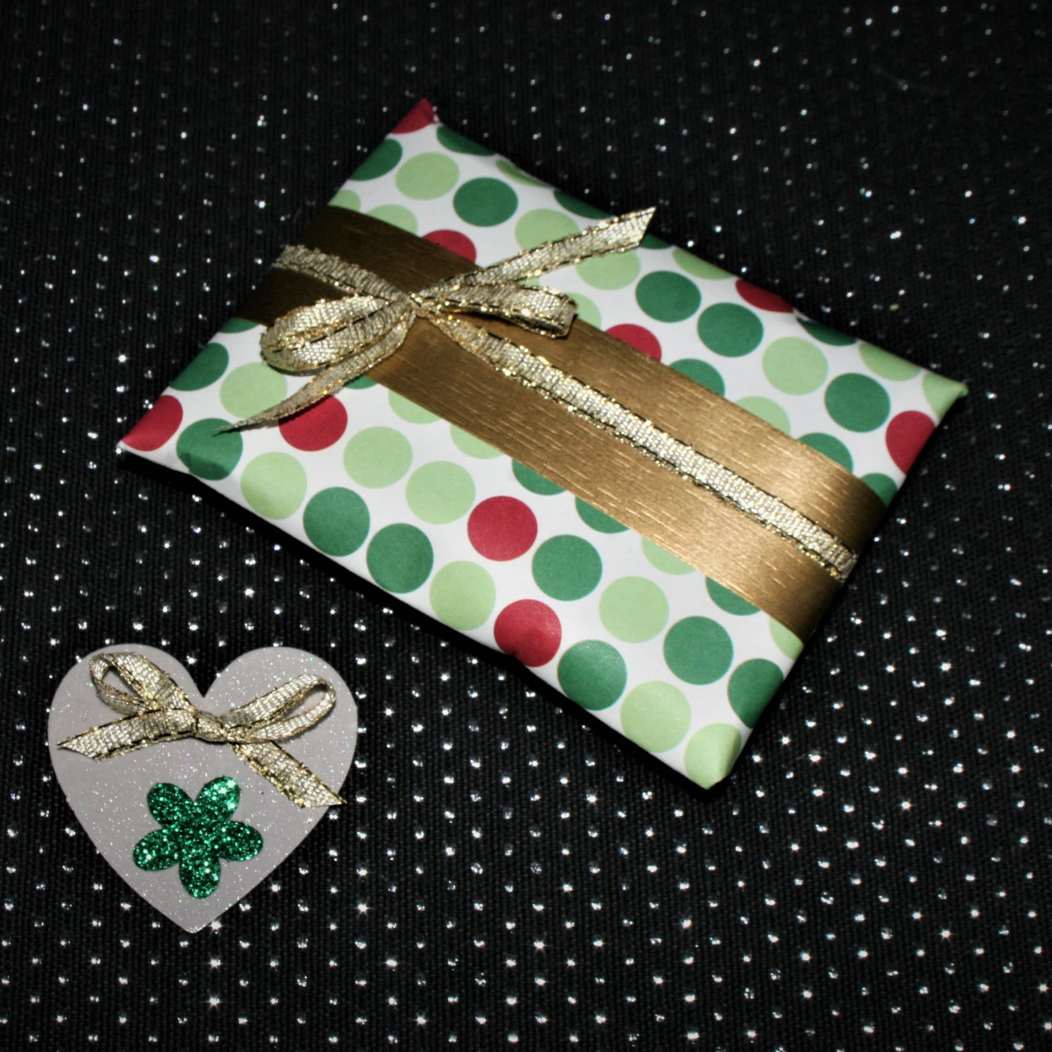 Gift box with polka dot paper, gold ribbon, and heart-shaped decoration on black background