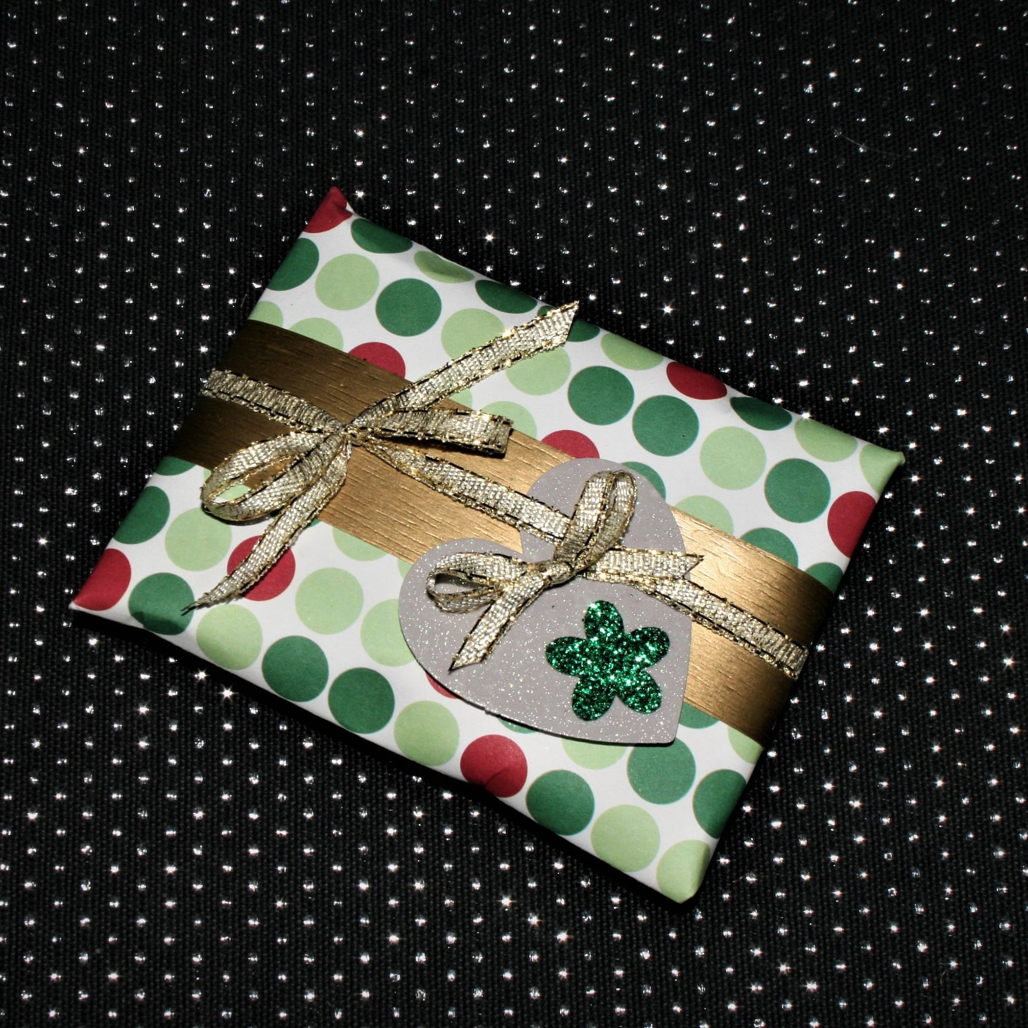 Gift wrapped in polka dot paper with gold ribbon and heart embellishment on black background