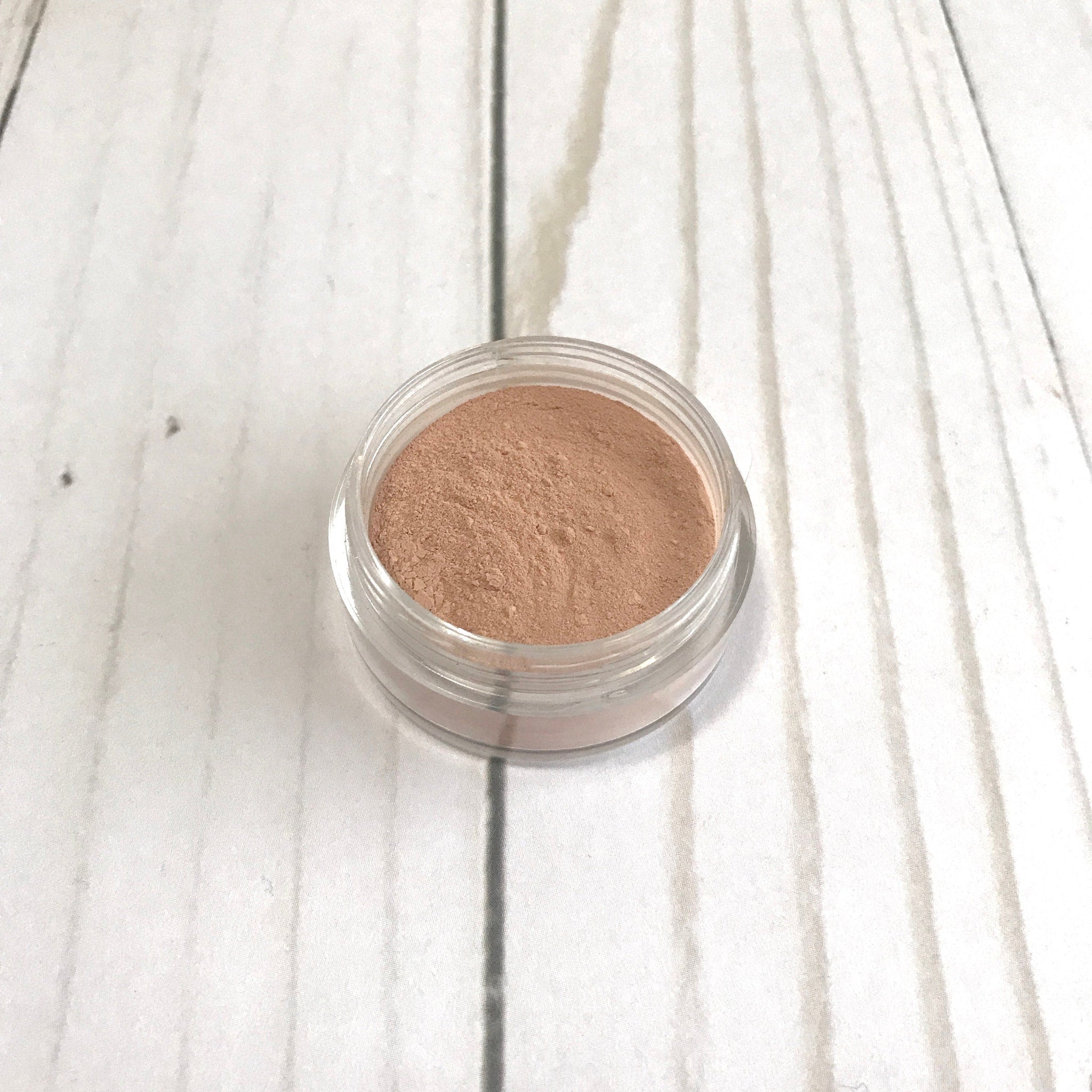 Loose mineral contour in clear jar with light brown powder on white wood background