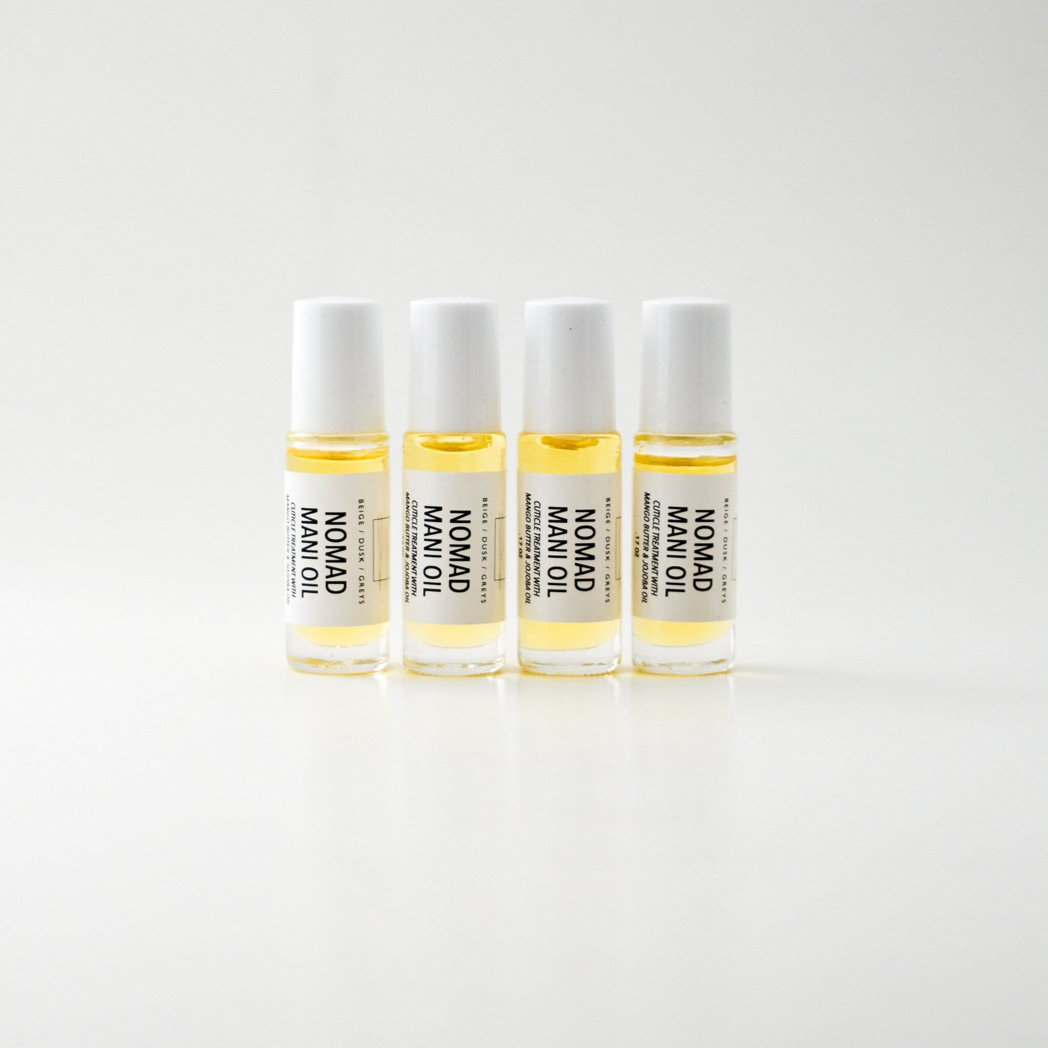 Mani oil bottles with white caps, clear glass, and NOMAD label, arranged on white surface
