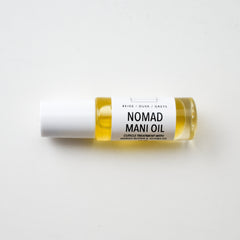 Mani oil bottle with white cap, clear glass, and yellow liquid, Nomad brand visible