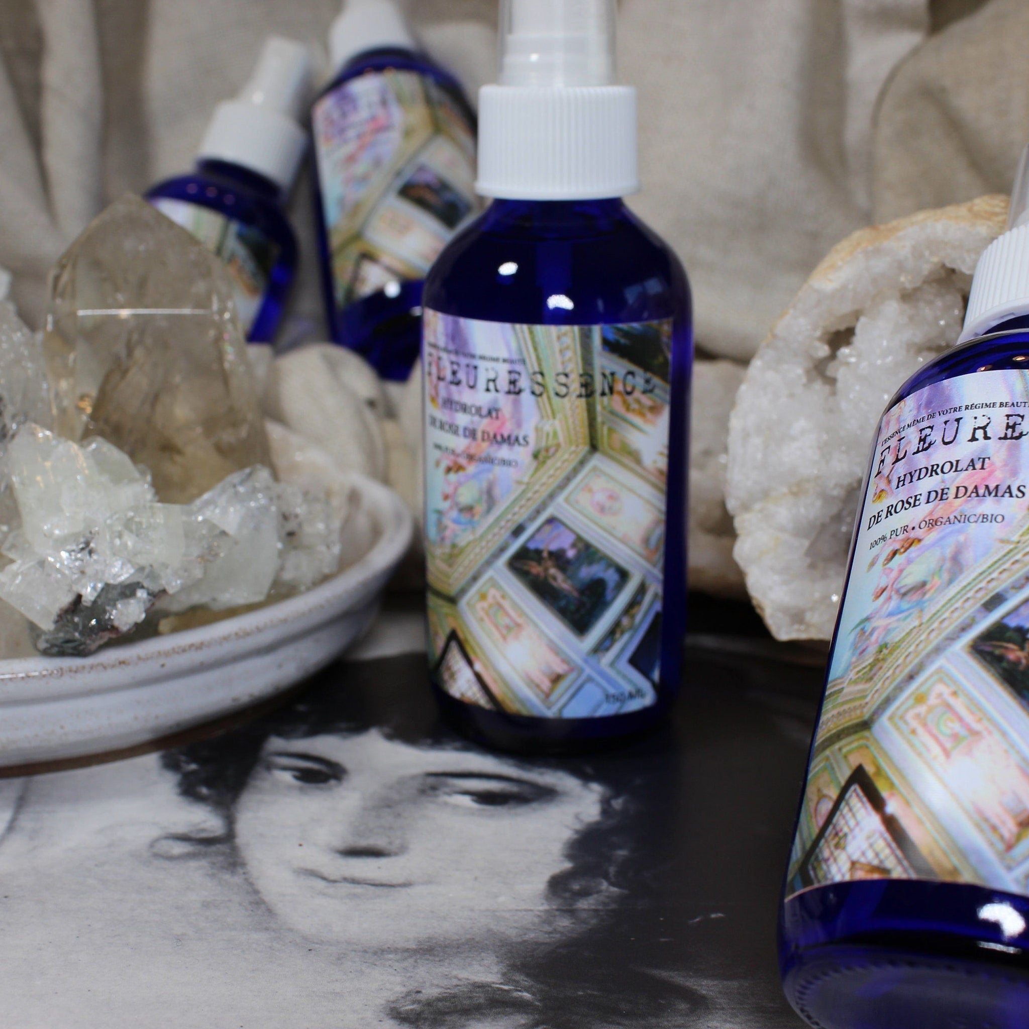 Blue glass spray bottles with white tops, "FLEURESSENCE" label, and crystals in background