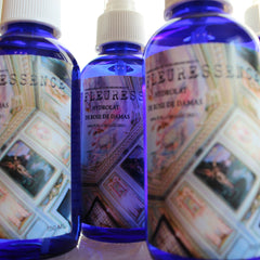 Spray bottles with blue glass, white spray tops, and patterned labels with "FLEURESSENCE" text visible