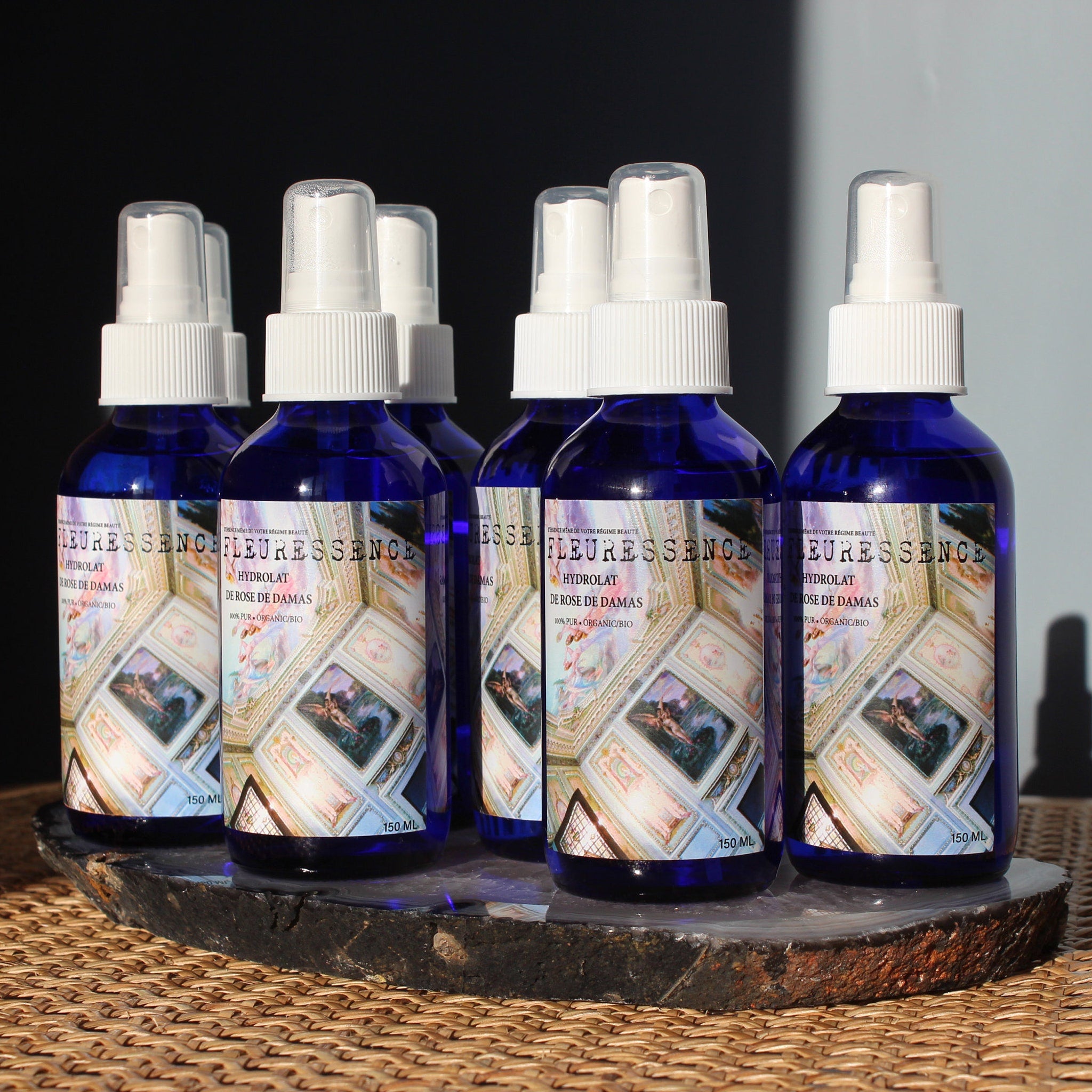 Blue glass spray bottles with white tops, "FLEURESSENCE" label, arranged on a stone slab