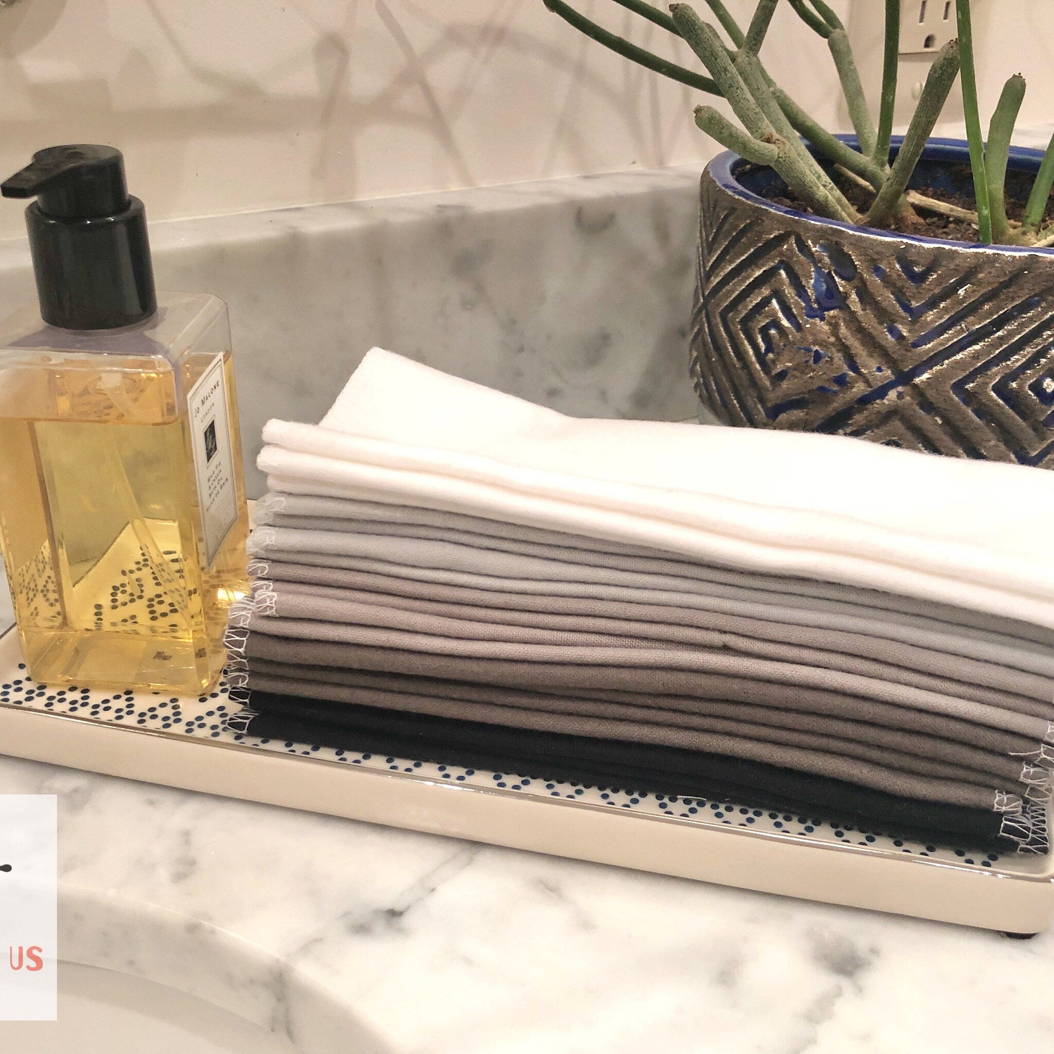 Stack of folded white, gray, and black cloths on a decorative tray next to soap bottle