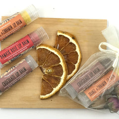 Lip balm tubes in various colors with Herbalicious label, on wood surface with dried orange slices