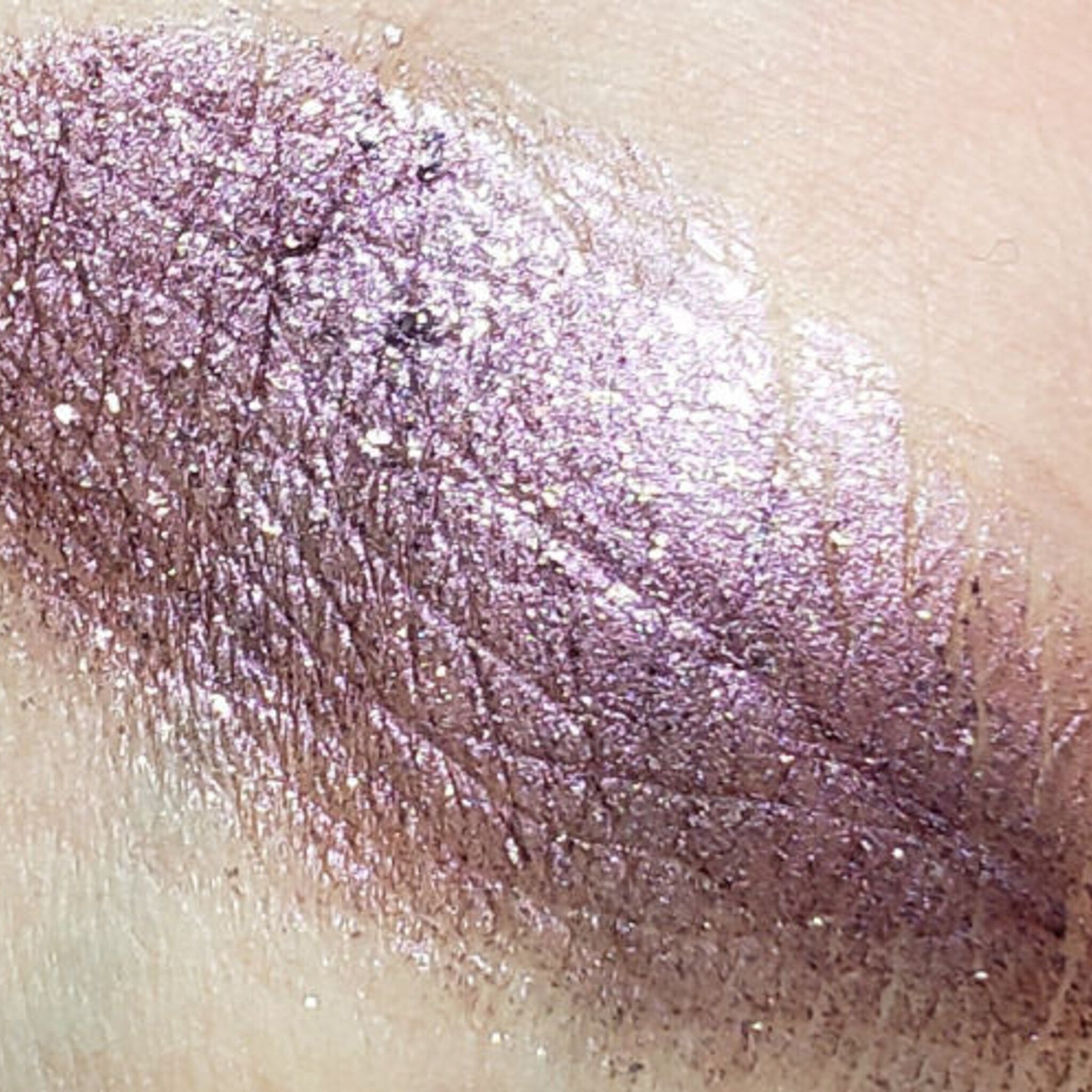Close-up of four shimmering eyeshadow pans in bronze, gold, rose, and plum with metallic finish