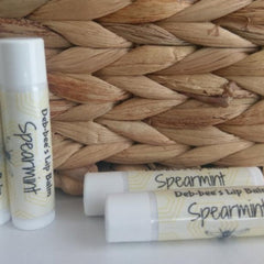 Lip balm tubes with white caps, Spearmint text, and Deb-bee's branding, against woven background