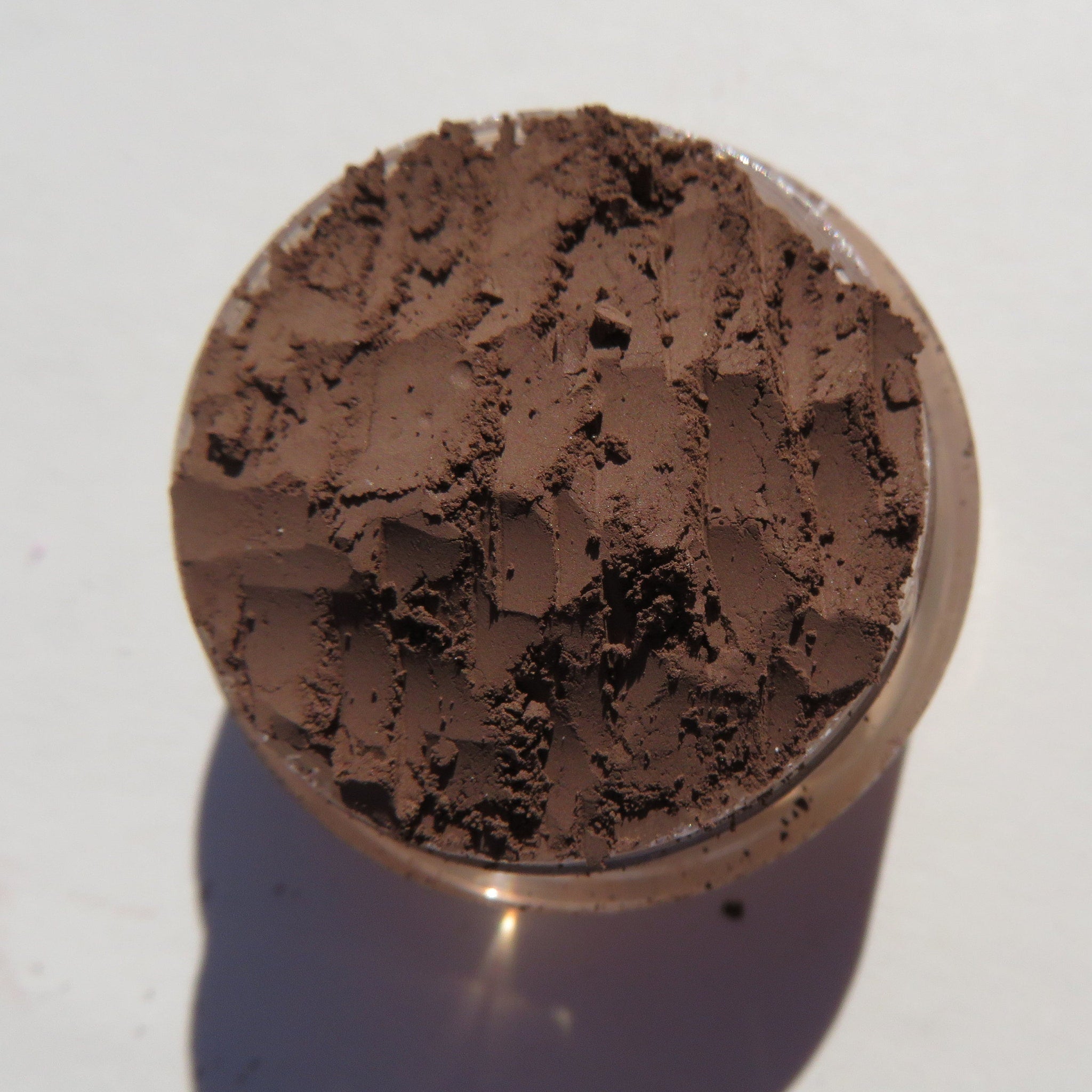 Brown powder makeup in a clear plastic container, textured surface, close-up view