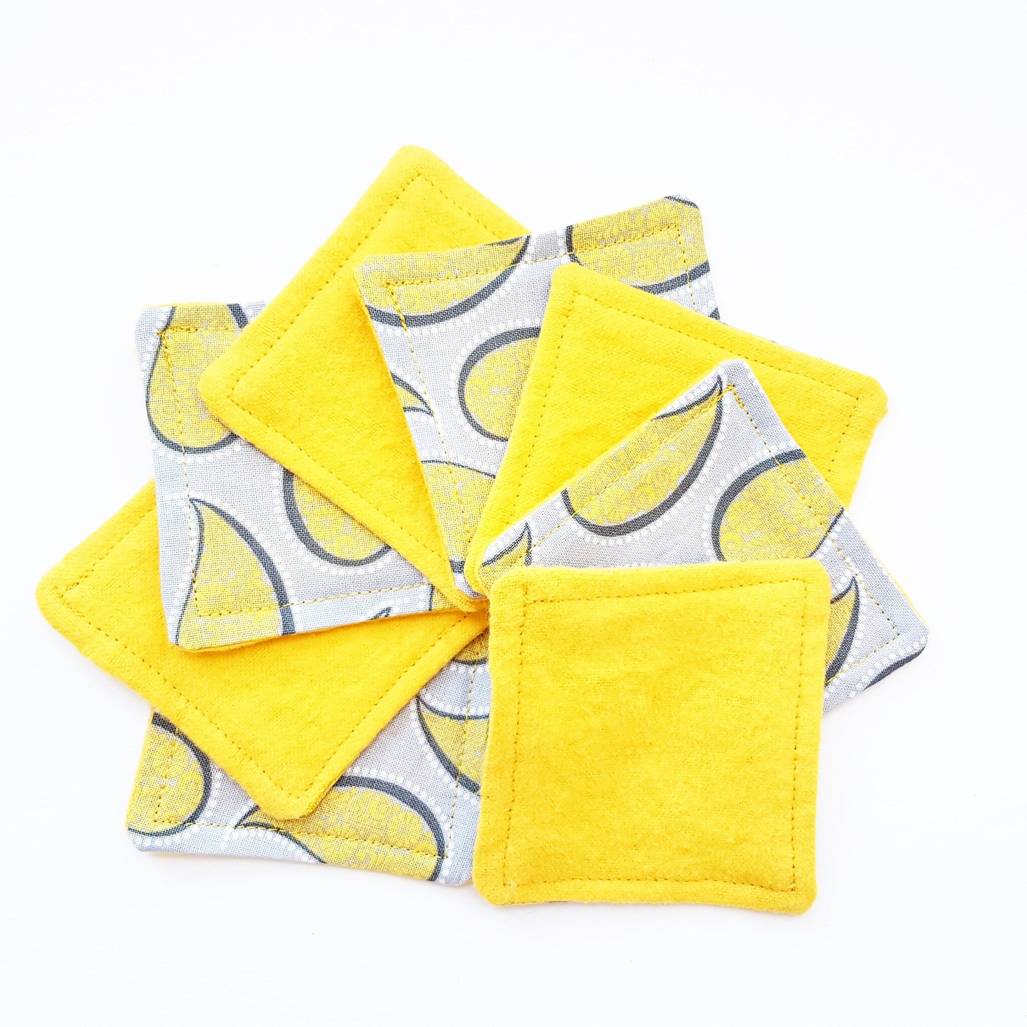 Coasters yellow fabric with lemon pattern and stitched edges, stacked on white surface