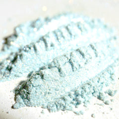 Close-up of iridescent turquoise and orange eye shadow with shimmering flecks in compact pan
