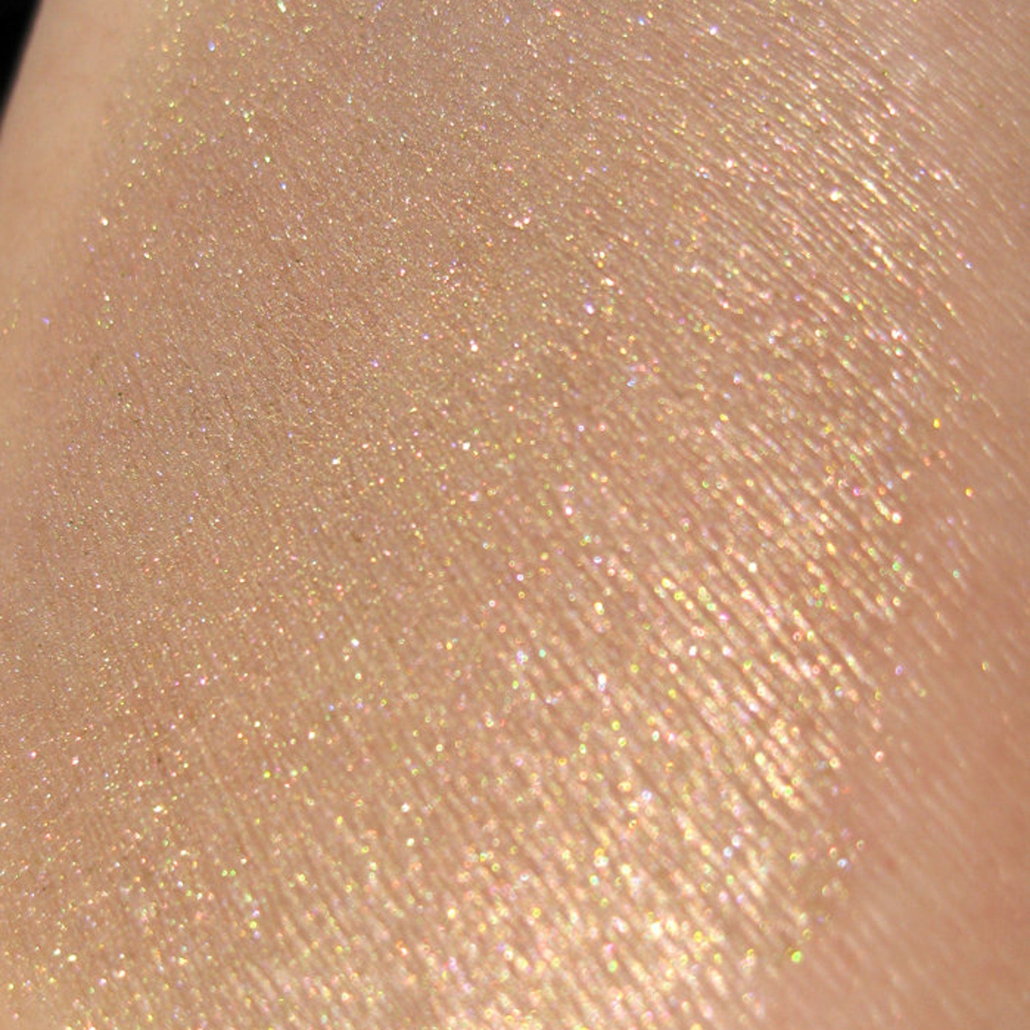 Side view of loose mineral eyeshadow in sheer tan with gold and green pearl shimmer, showcasing silky texture