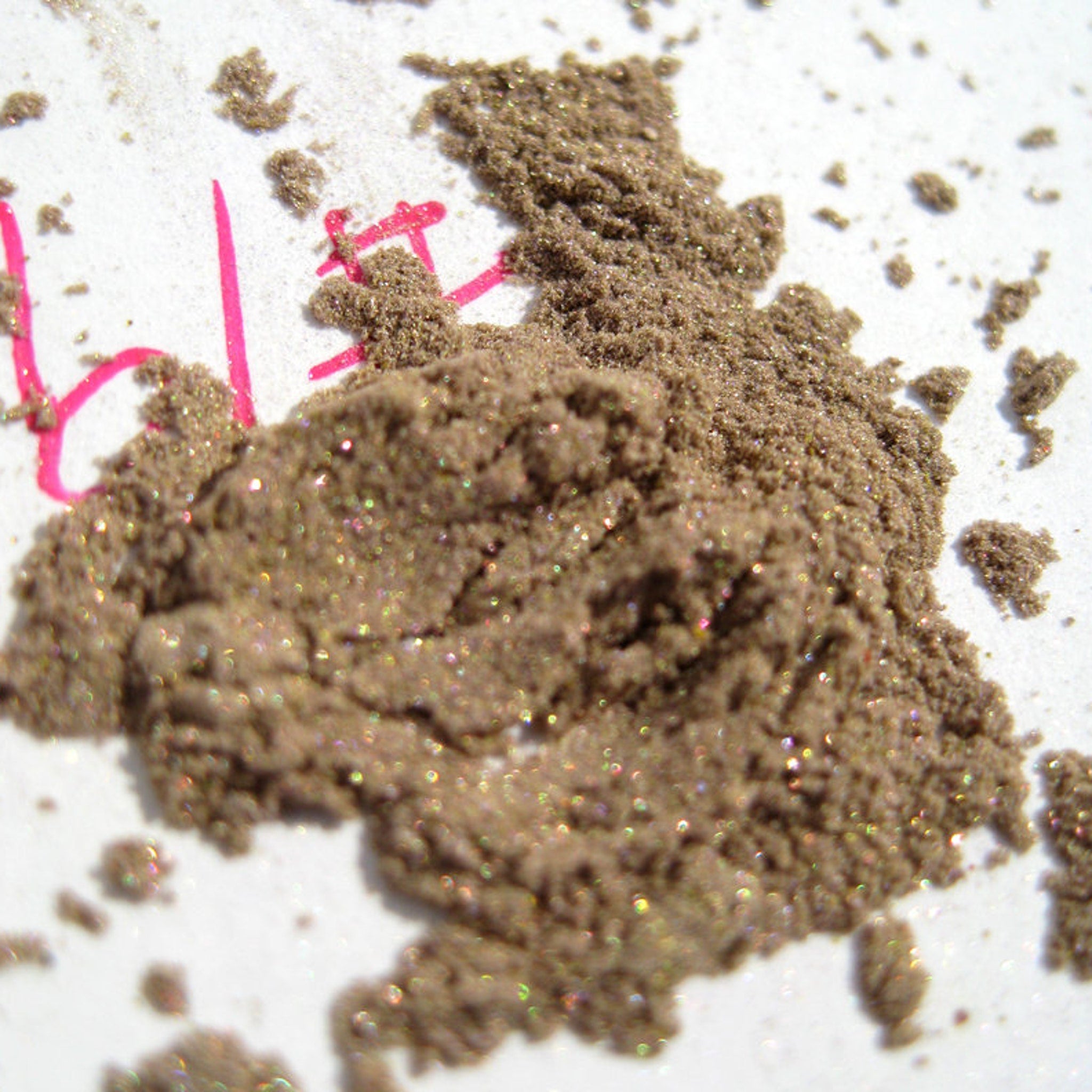 Close-up of loose mineral eyeshadow in neutral taupe beige with gold and green pearl shimmer, vegan silk finish
