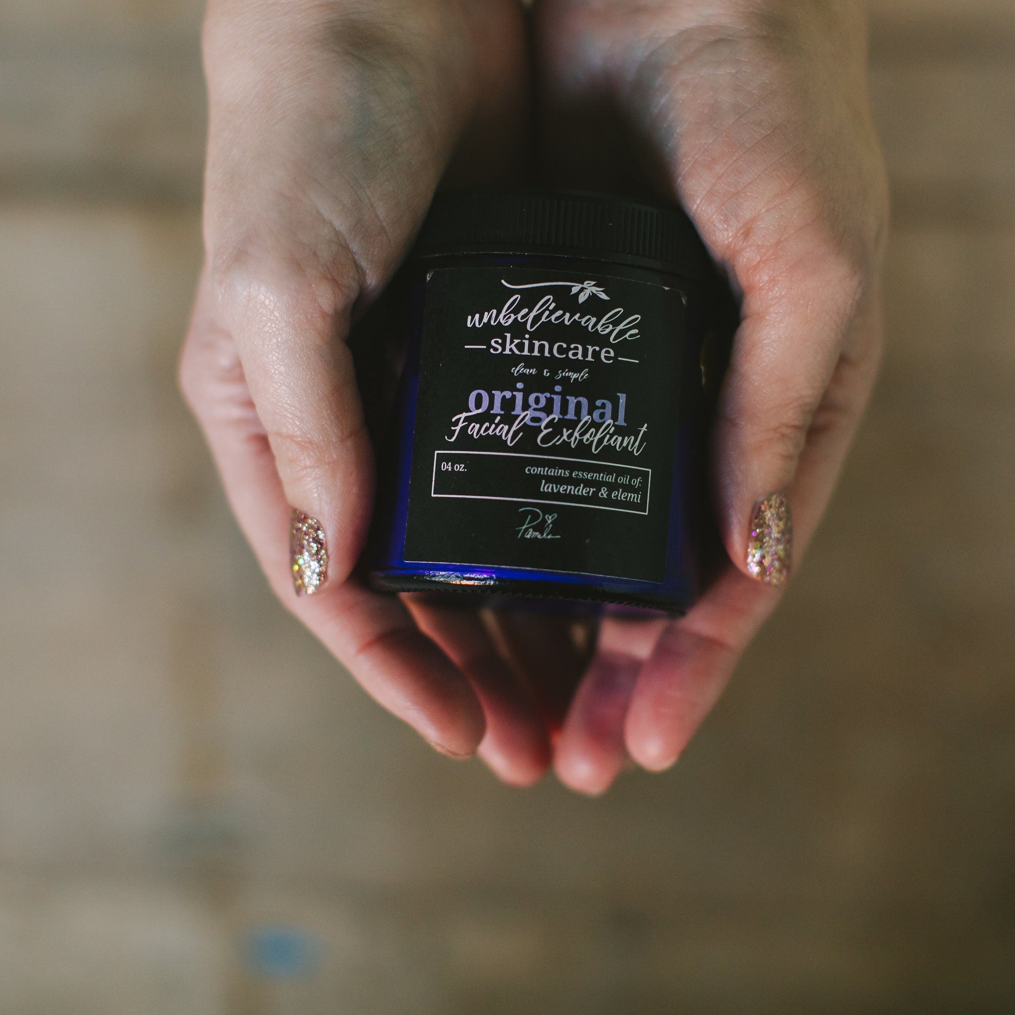 Facial Exfoliant jar with blue label, black cap, and hands holding it, "Unbelievable Skincare" visible