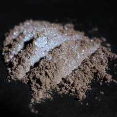 Side view of taupe eyeshadow pan with beige base and silver-blue shimmer particles catching light