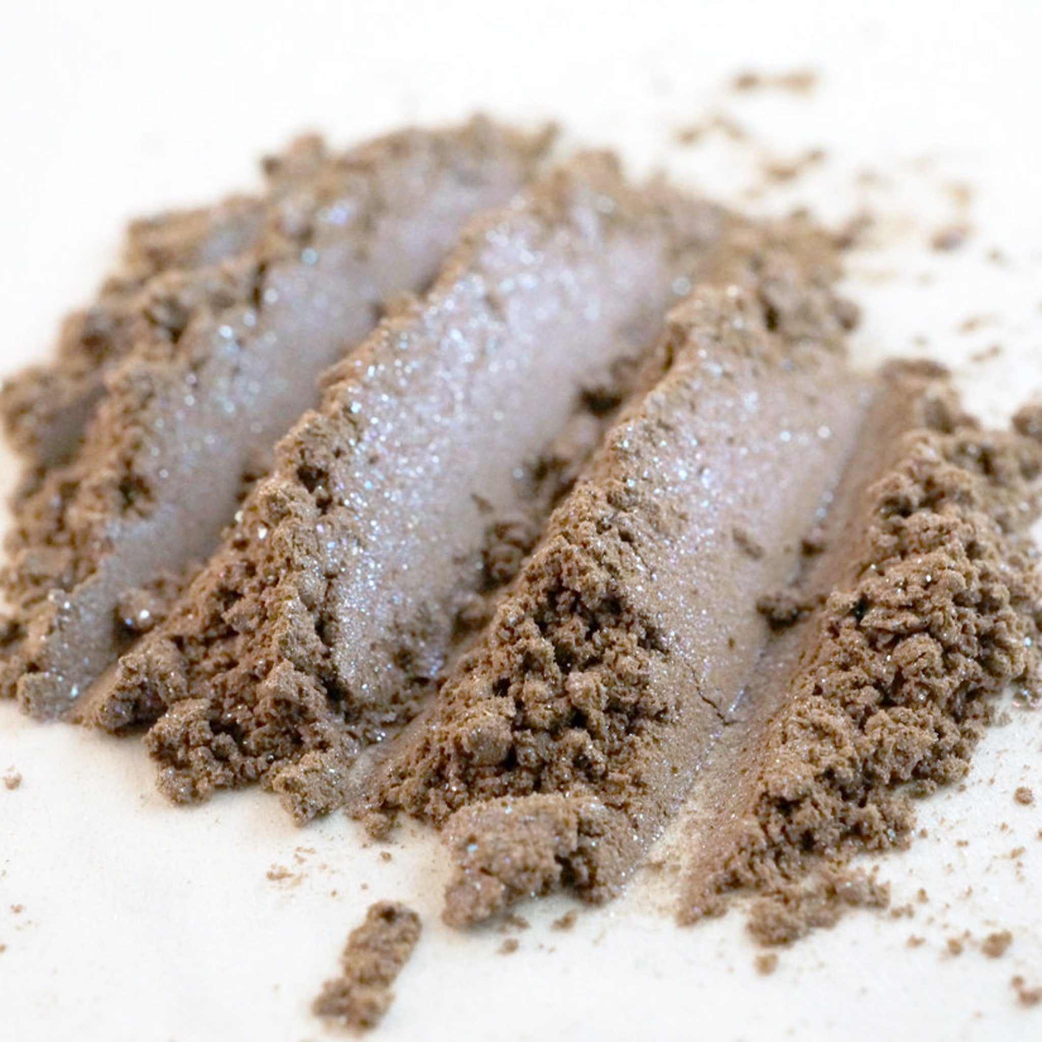 Close-up of taupe eyeshadow pan with silver and iridescent blue shimmer particles catching light