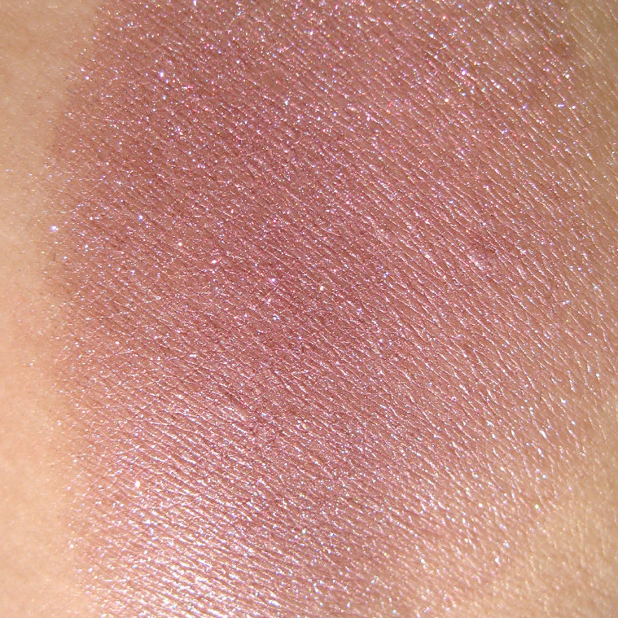 Pink glitter eyeshadow swatch with shimmer and skin texture visible on the arm