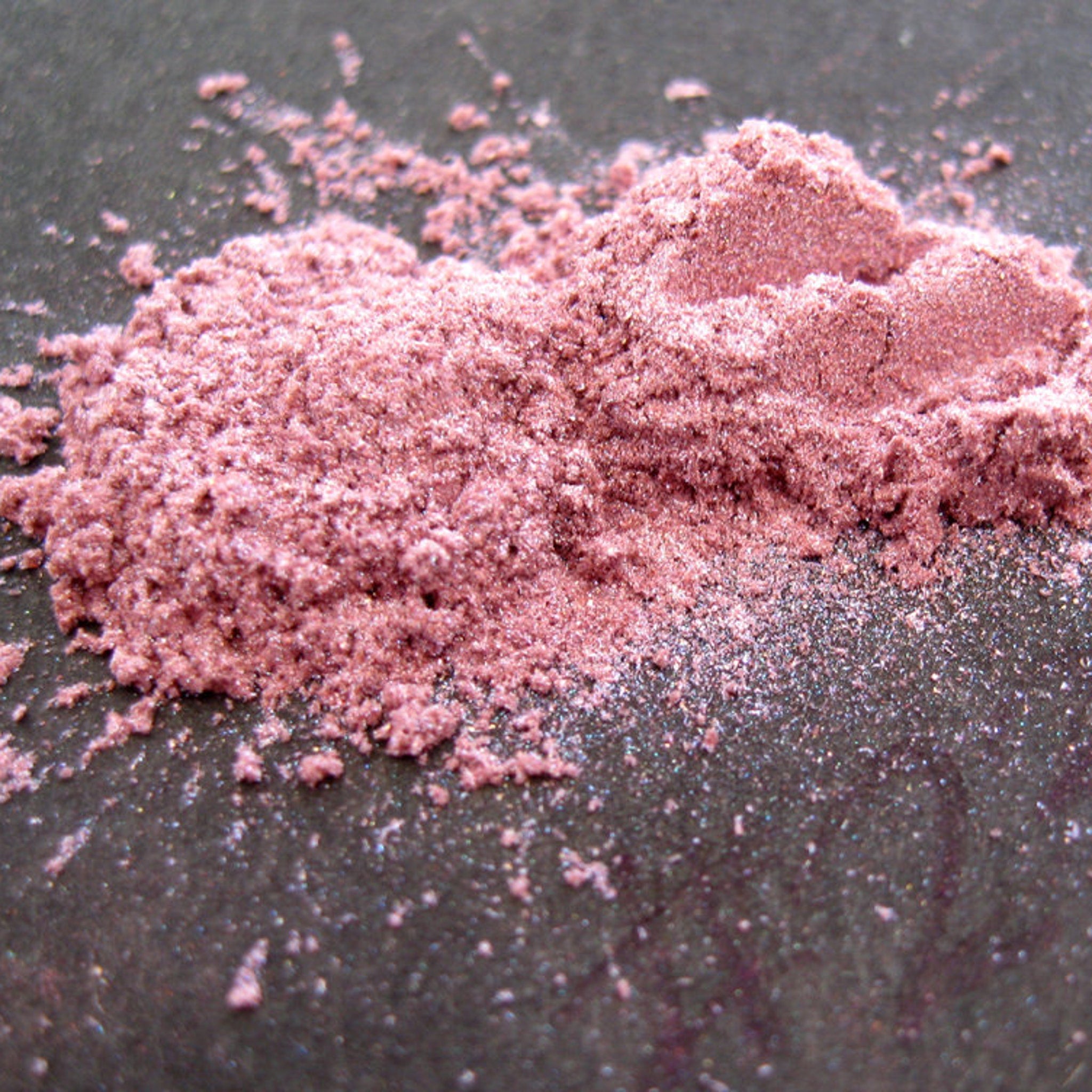 Pink powder pigment with granular texture on dark surface