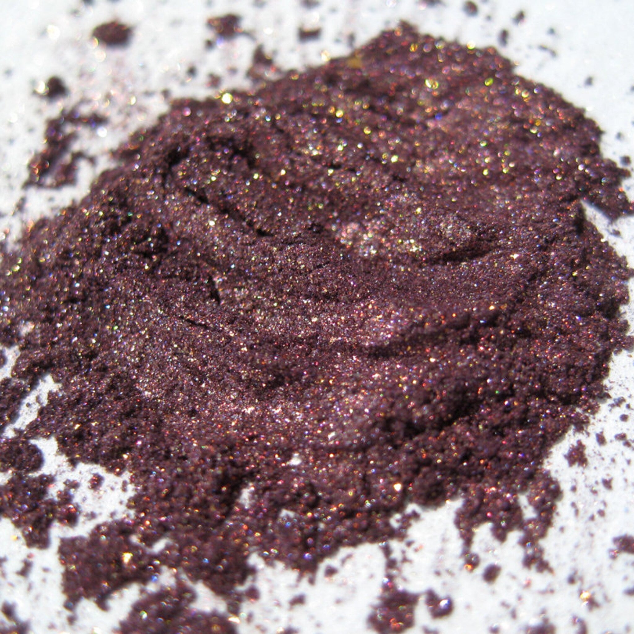 Close-up swatch of warm metallic plum eyeshadow with iridescent copper shimmer and glitter particles