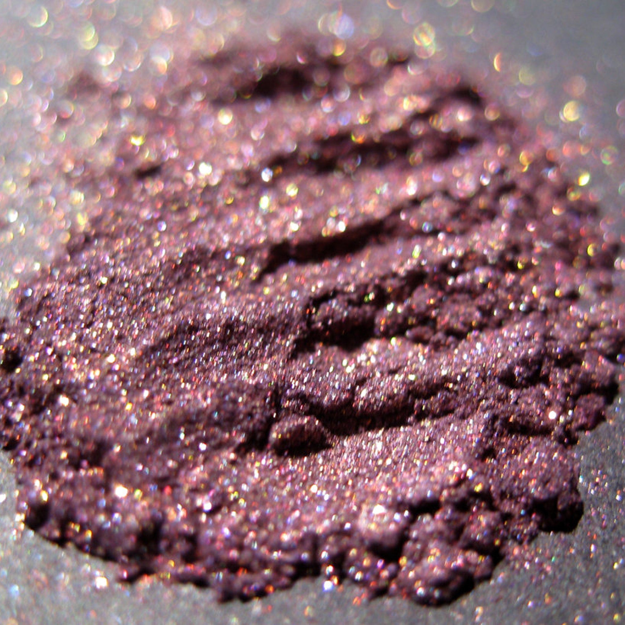 Side view of warm metallic purple eyeshadow pan with iridescent copper shimmer and glitter particles catching light