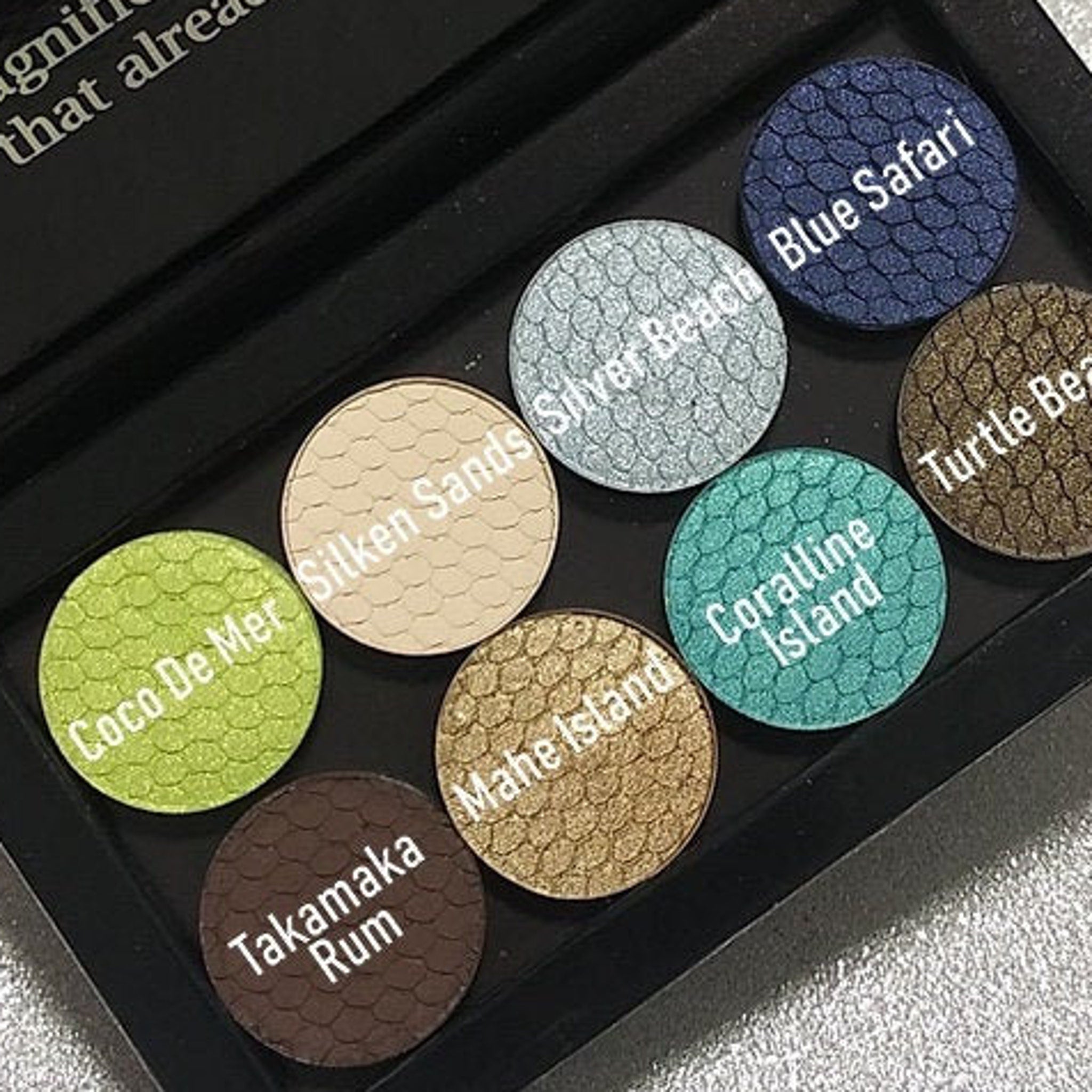Eyeshadow palette with various colors and textures, including green, blue, brown, and gold shades with text labels