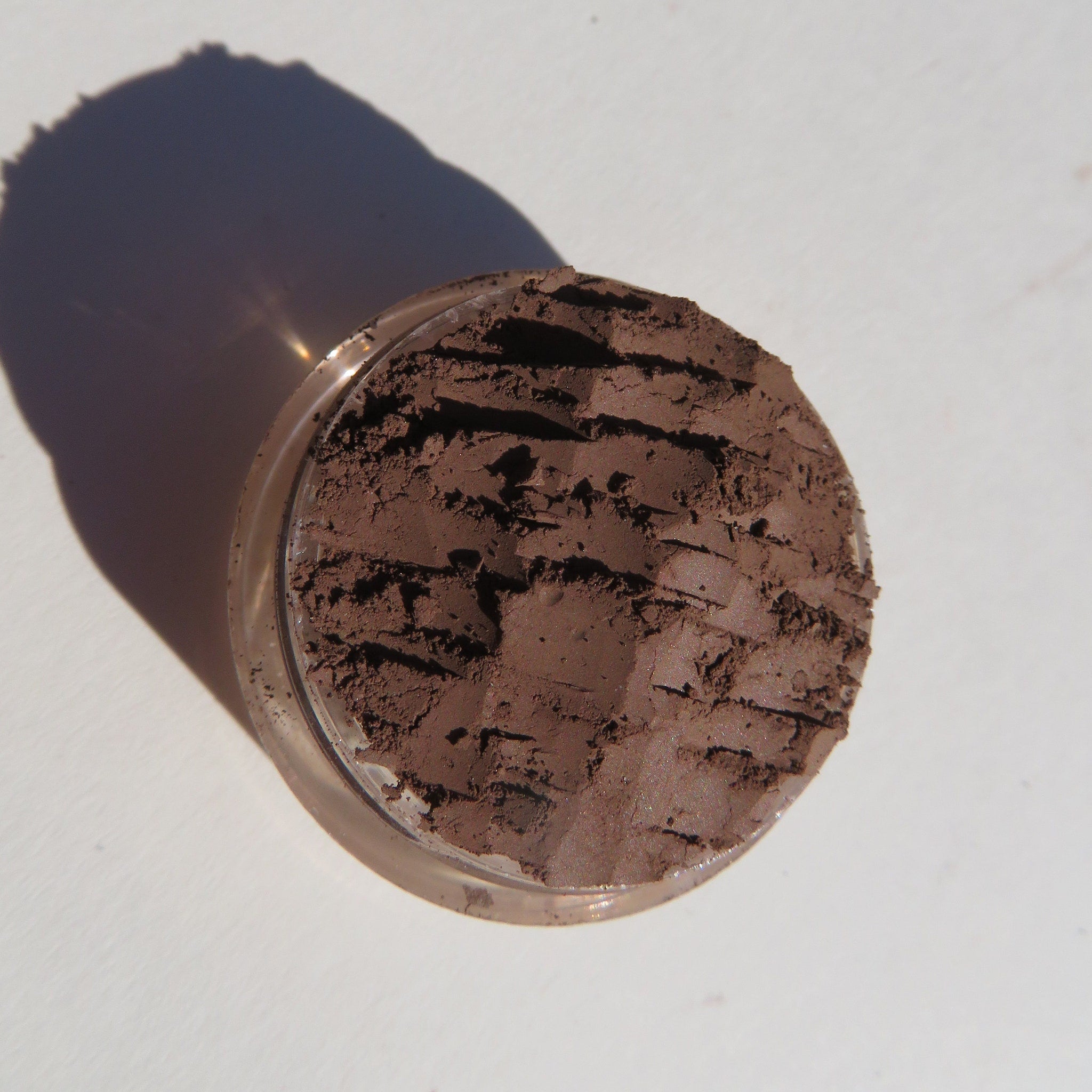 Side view of dark matte brown mineral eye shadow in loose powder form with vegan certification label visible