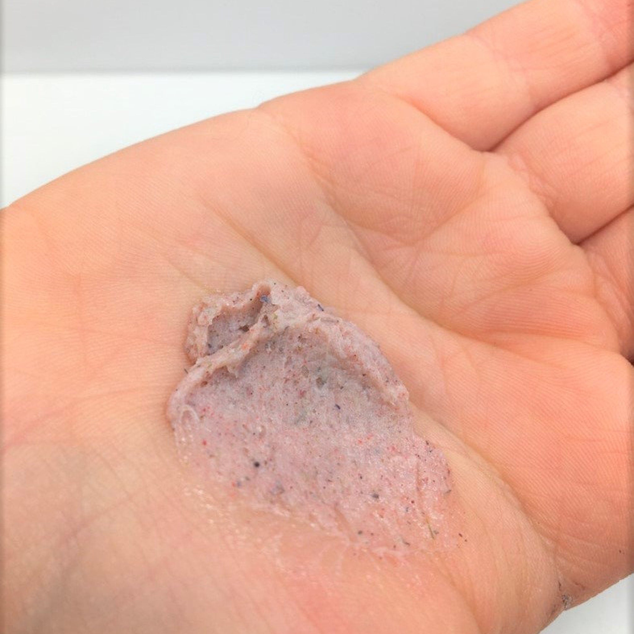 Exfoliating scrub in hand, pink and speckled texture, close-up view