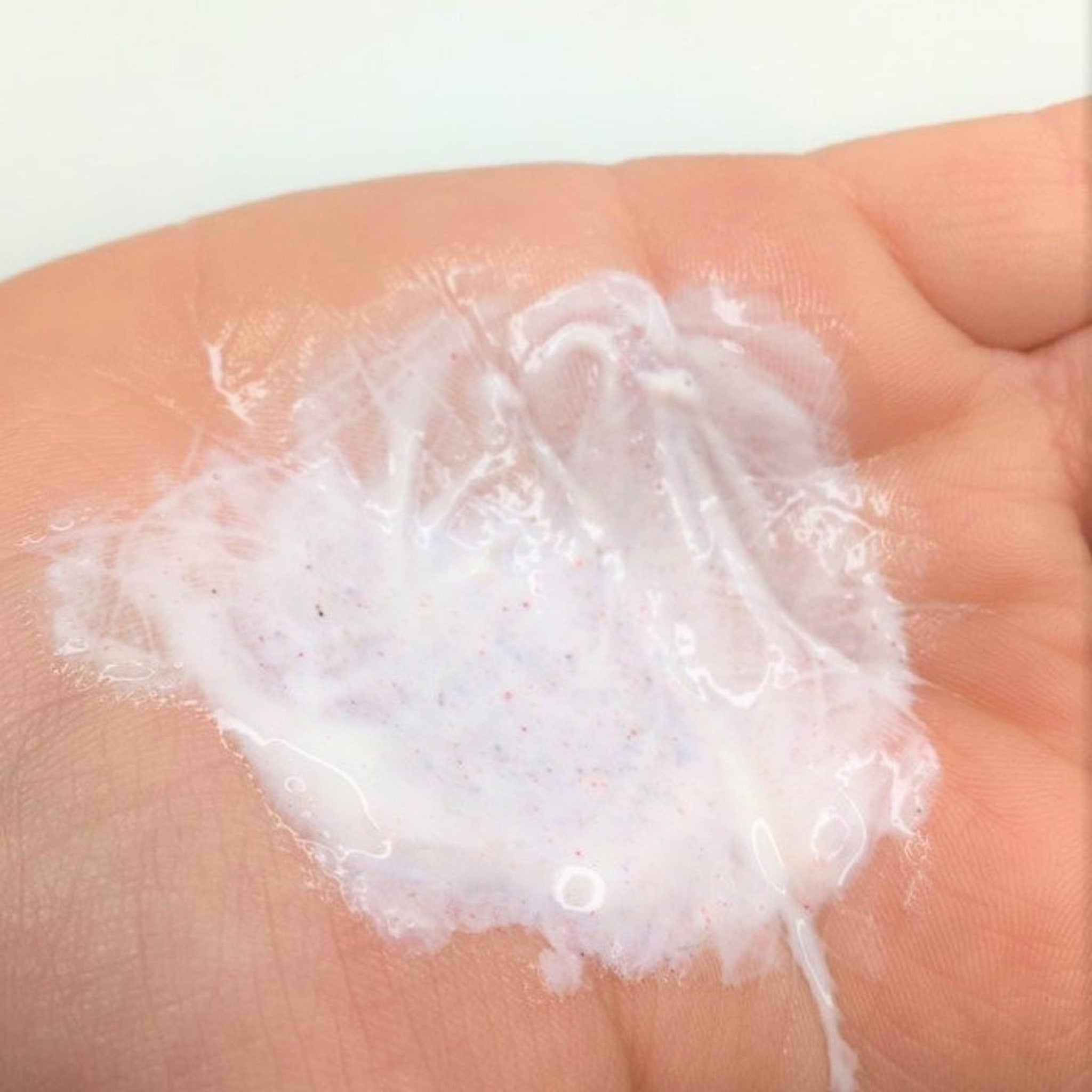 White lotion with red specks on skin, close up view of hand