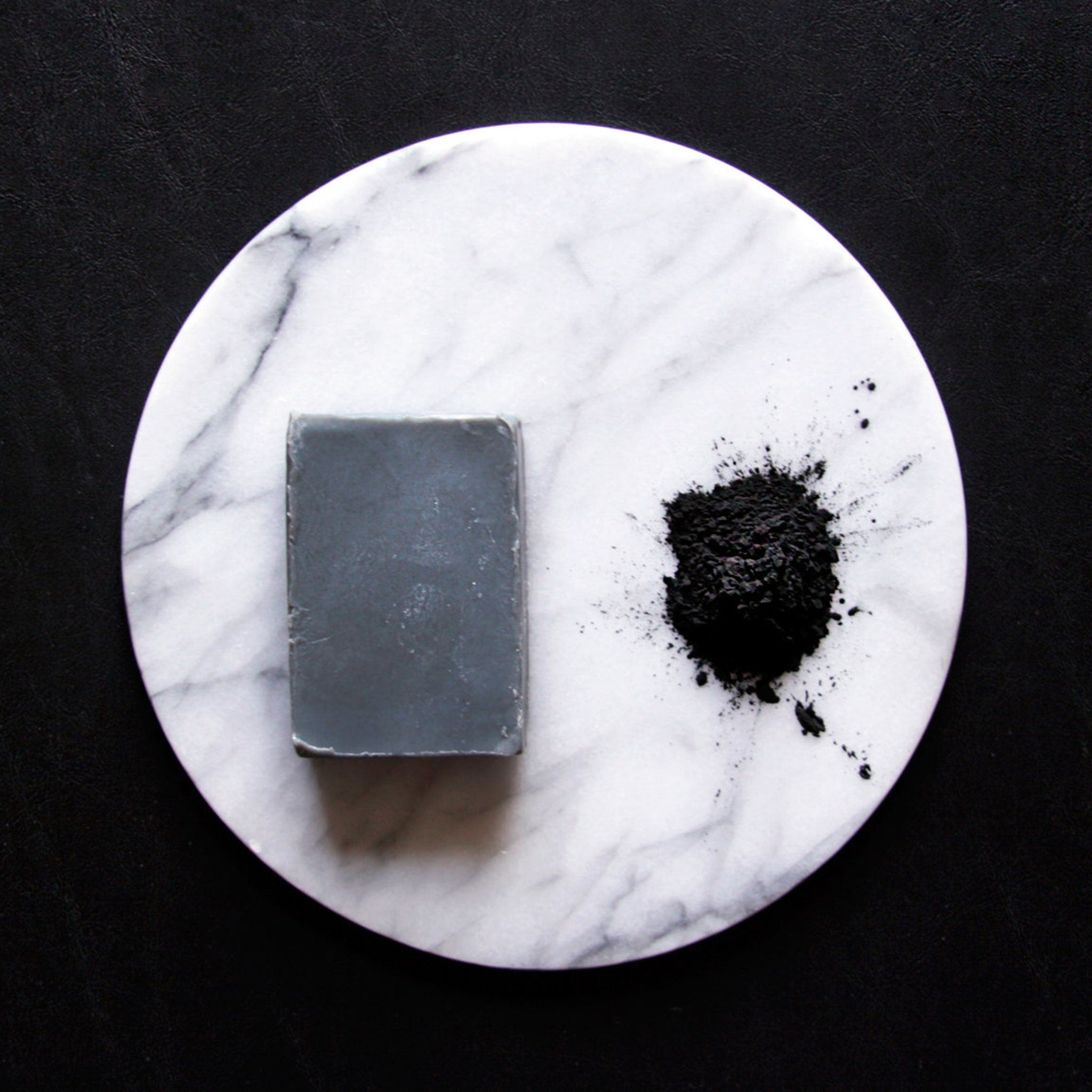 Soap bar and powder on white marble with black background, gray soap, black powder, and marble pattern