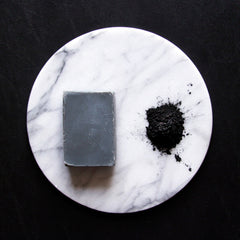 Soap bar and powder on white marble with black background, gray soap, black powder, and marble pattern